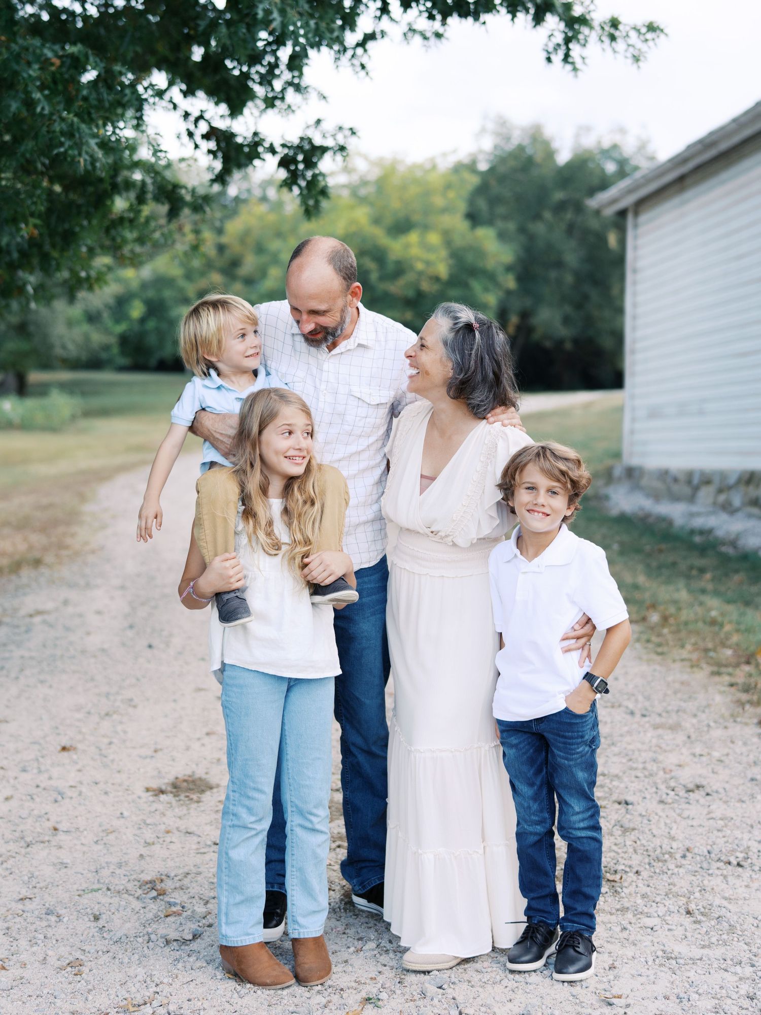 A family shares joyful moments together on a gravel path near a white building on a sunny day.