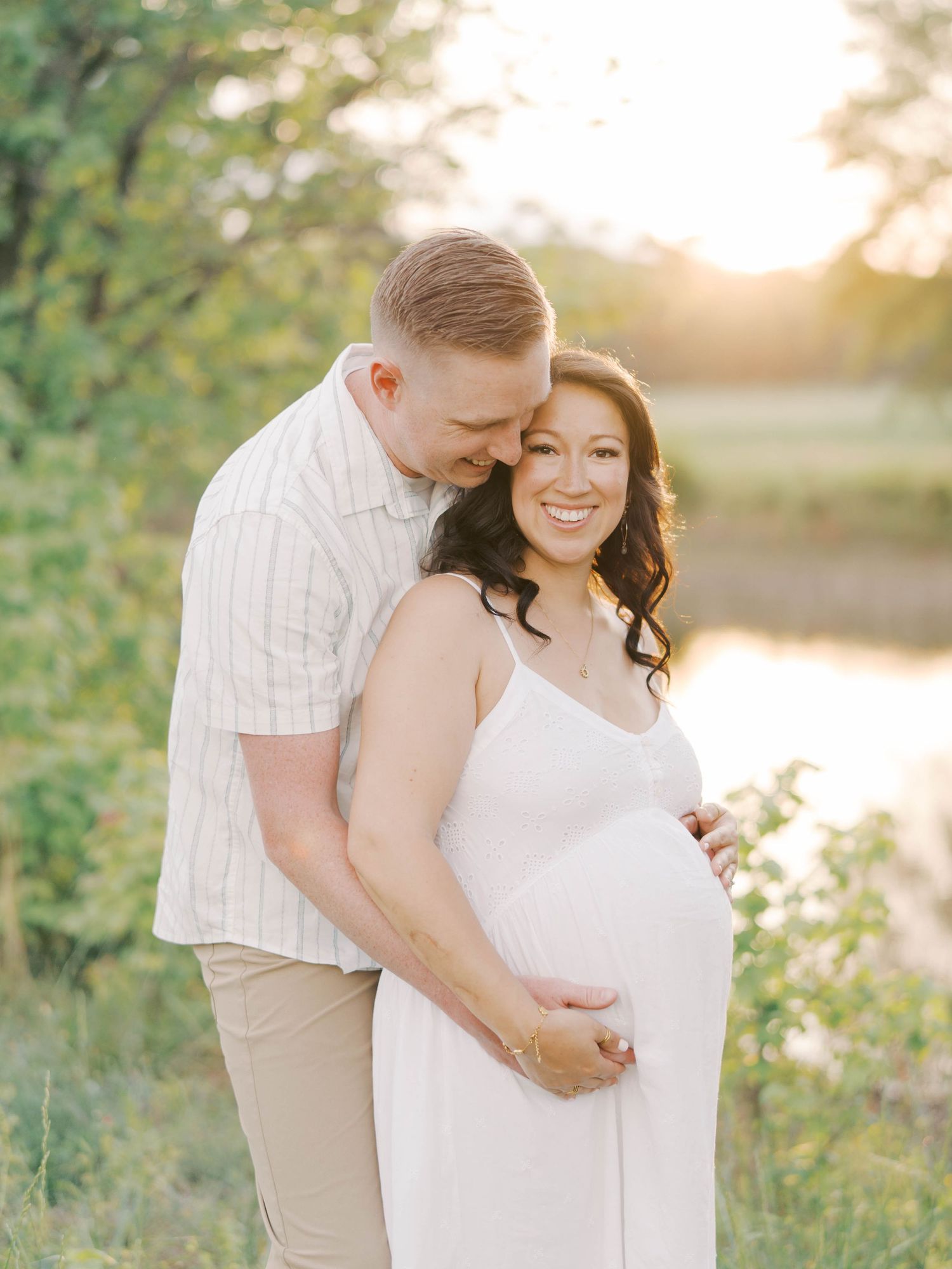 Couple embraces tenderly in a golden field at sunset as they celebrate their pregnancy.