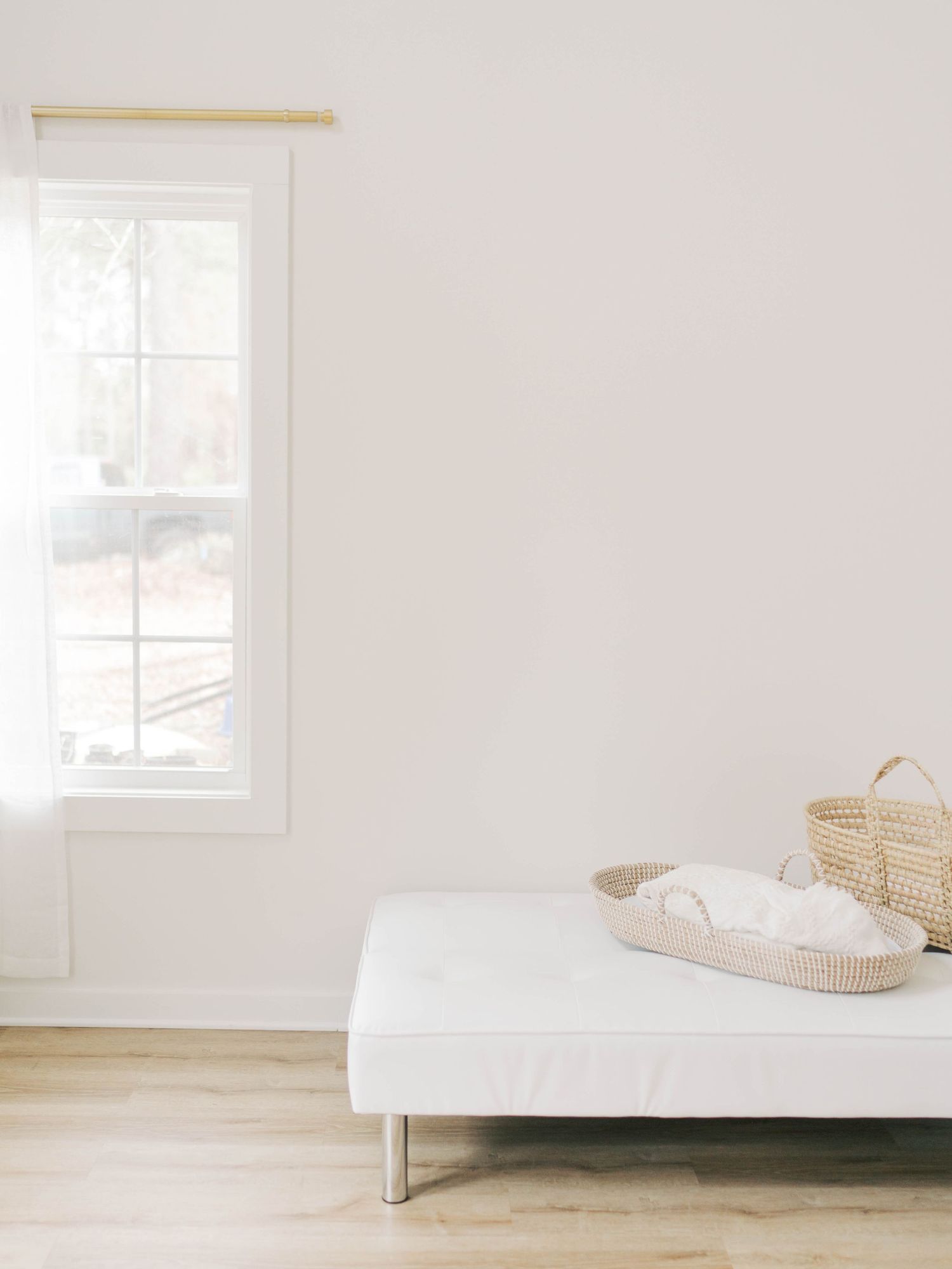 Minimalist white bedroom with window, wooden floor, and woven baskets on a modern daybed.