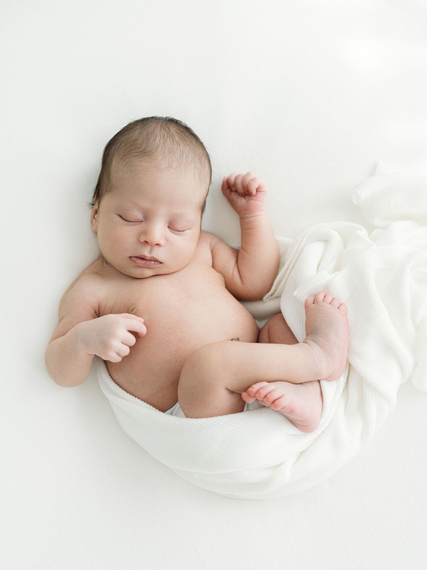Peaceful sleeping newborn baby wrapped in soft white fabric on a white background.