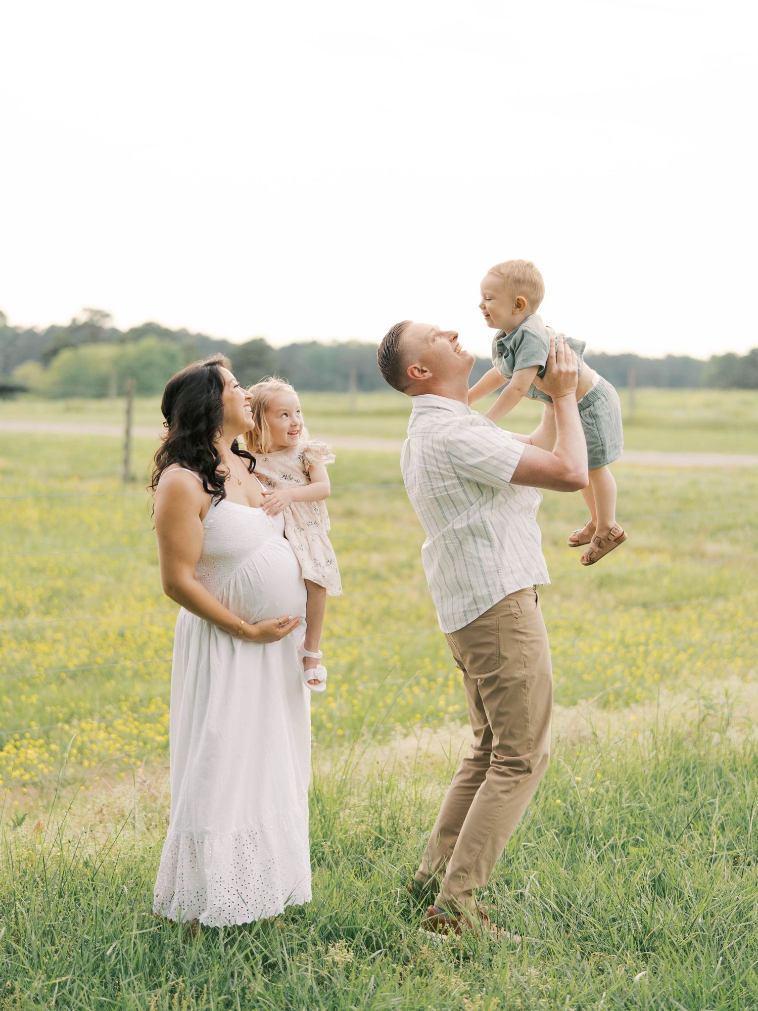 Family sharing joyful moment in sunny meadow during maternity photoshoot.