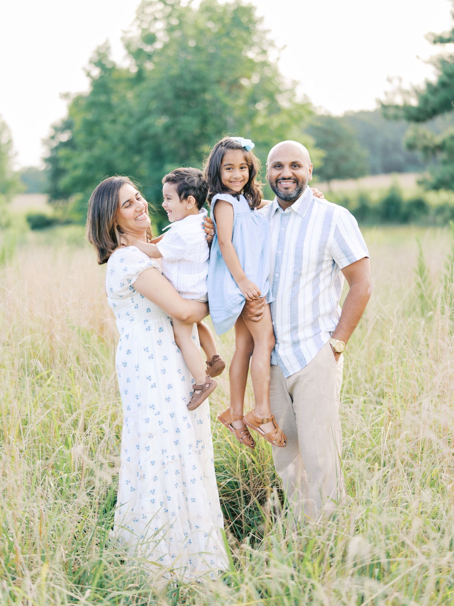 Family enjoying a tender moment together in a sunlit meadow with tall grass during a summer photoshoot.