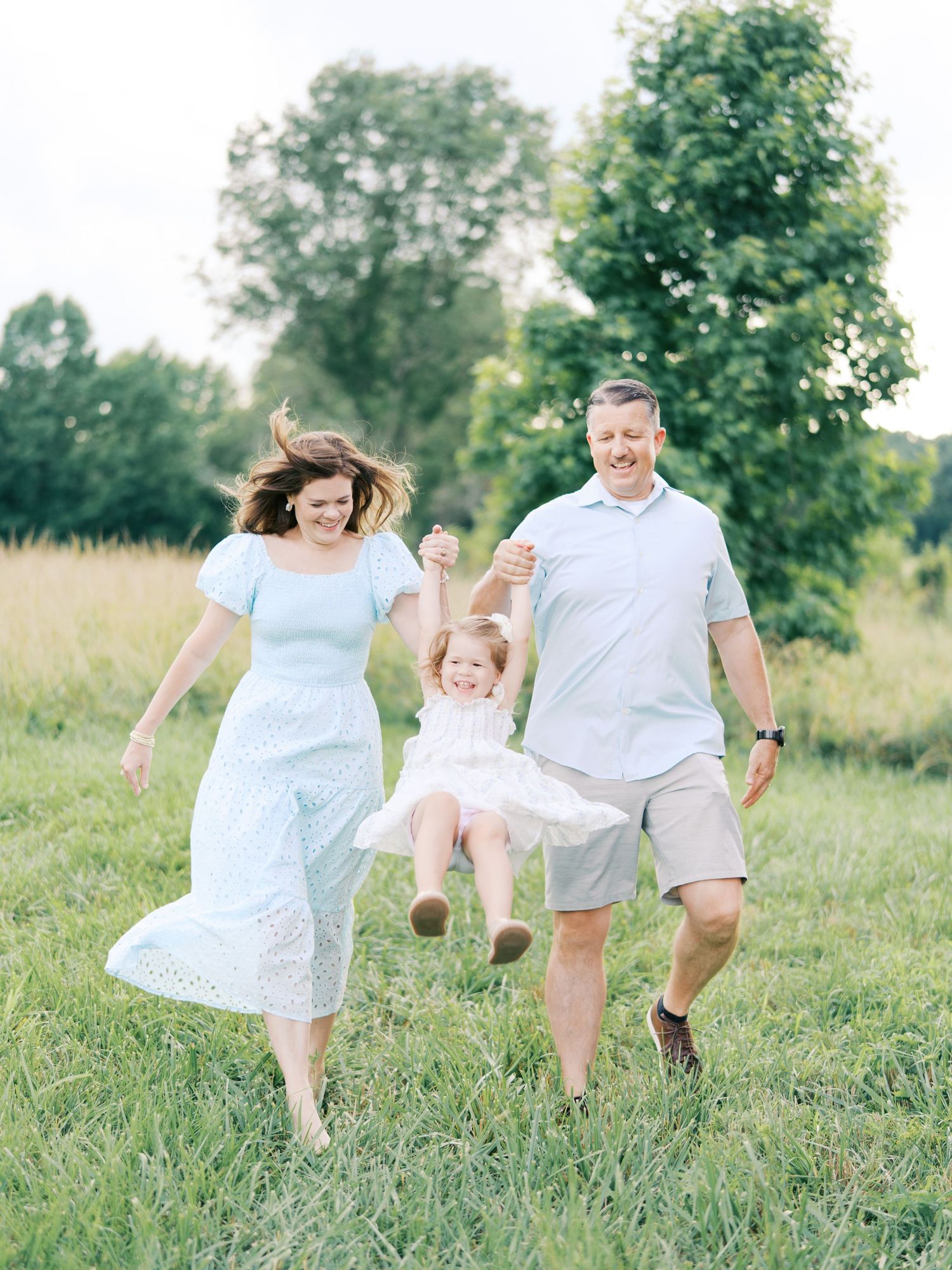 A playful family moment captured in a grassy field as they dance and laugh together in coordinated white outfits.