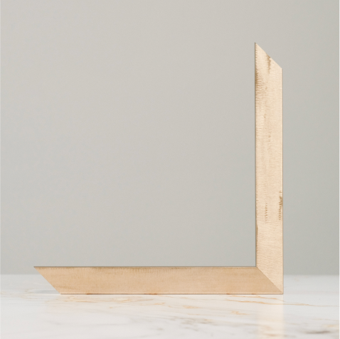 Natural wood picture frame corner detail displayed on marble surface against gray background.