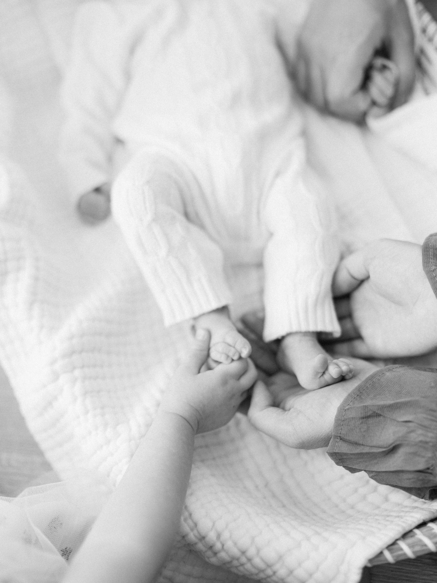 Black and white photo of parents gently holding their newborn baby's tiny hands, capturing a tender family moment.