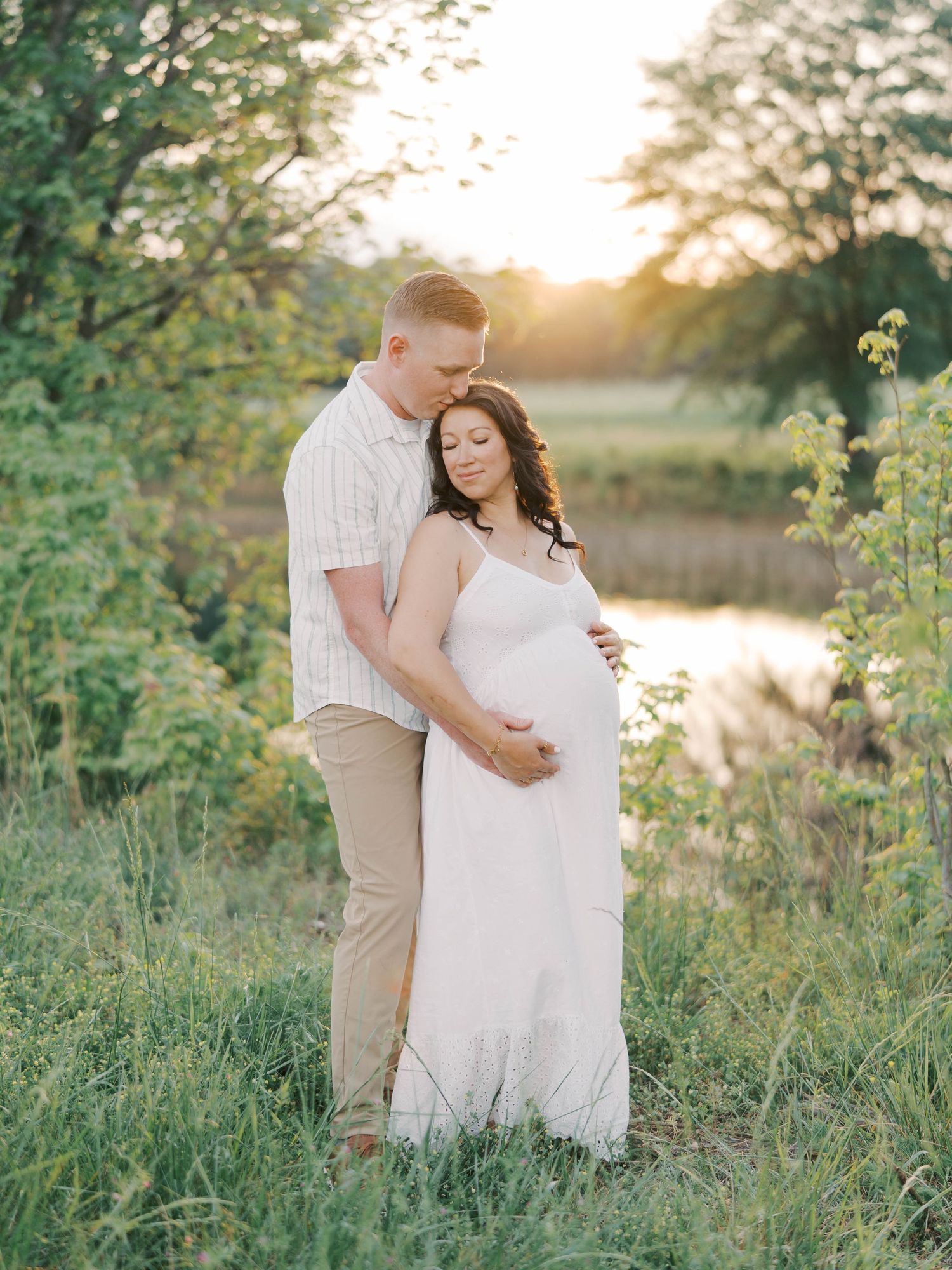 Romantic maternity photo of couple embracing at sunset by pond.