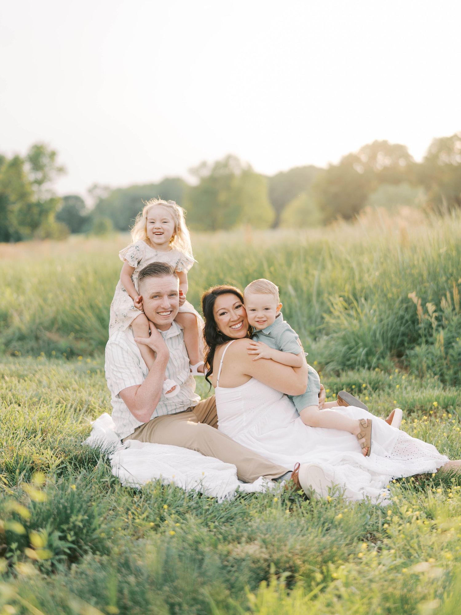 Family enjoying tender moments together while sitting in a sunlit meadow during golden hour.