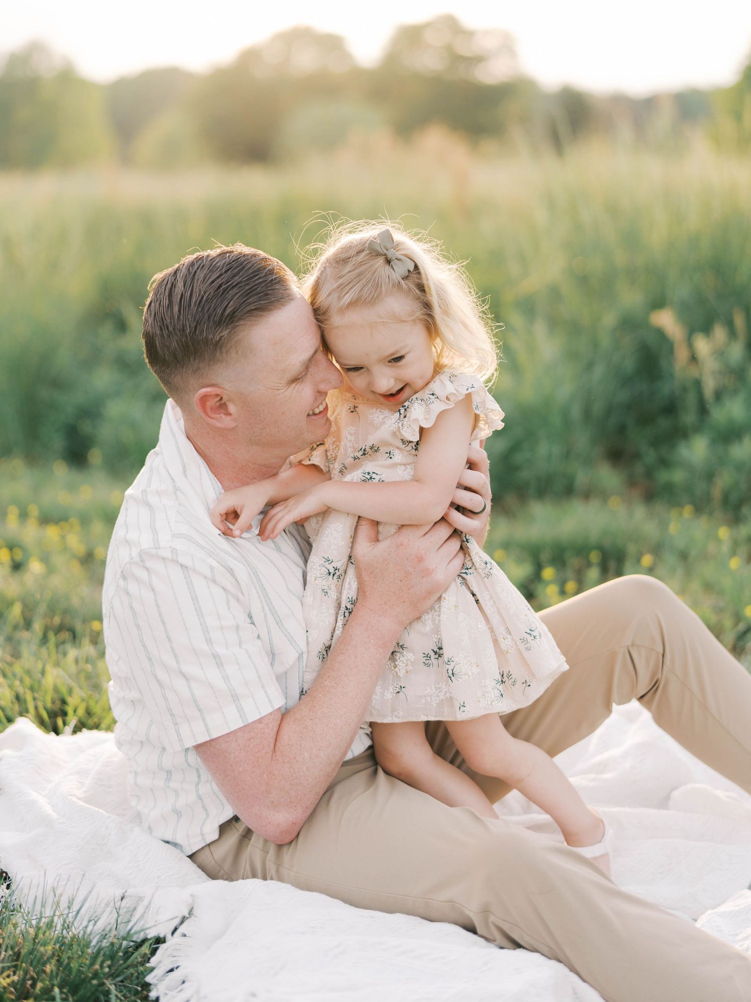 Sweet moment between parent and child sitting on white blanket in grassy meadow.