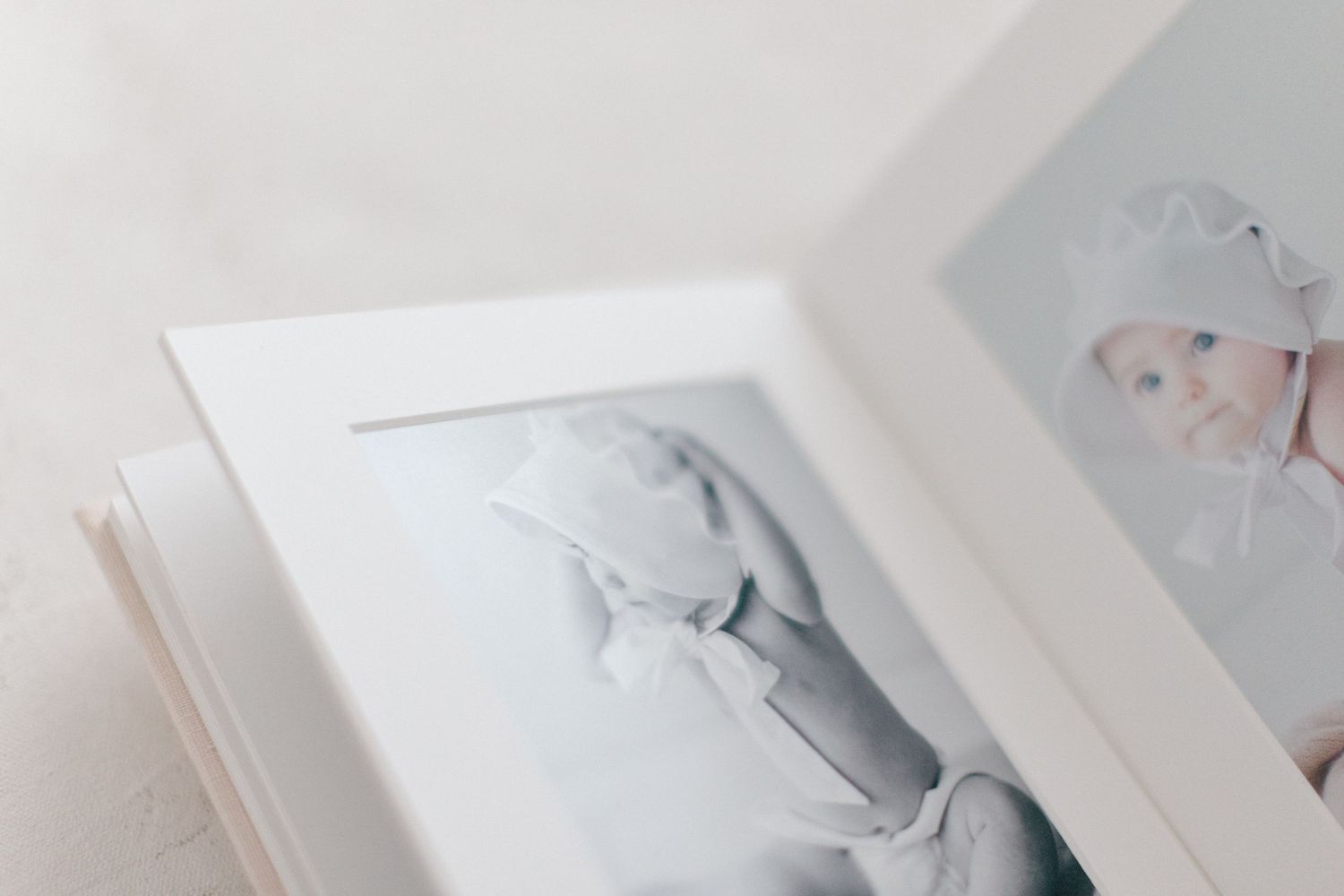 White framed photo album displaying soft newborn baby portraits in delicate pastel tones.