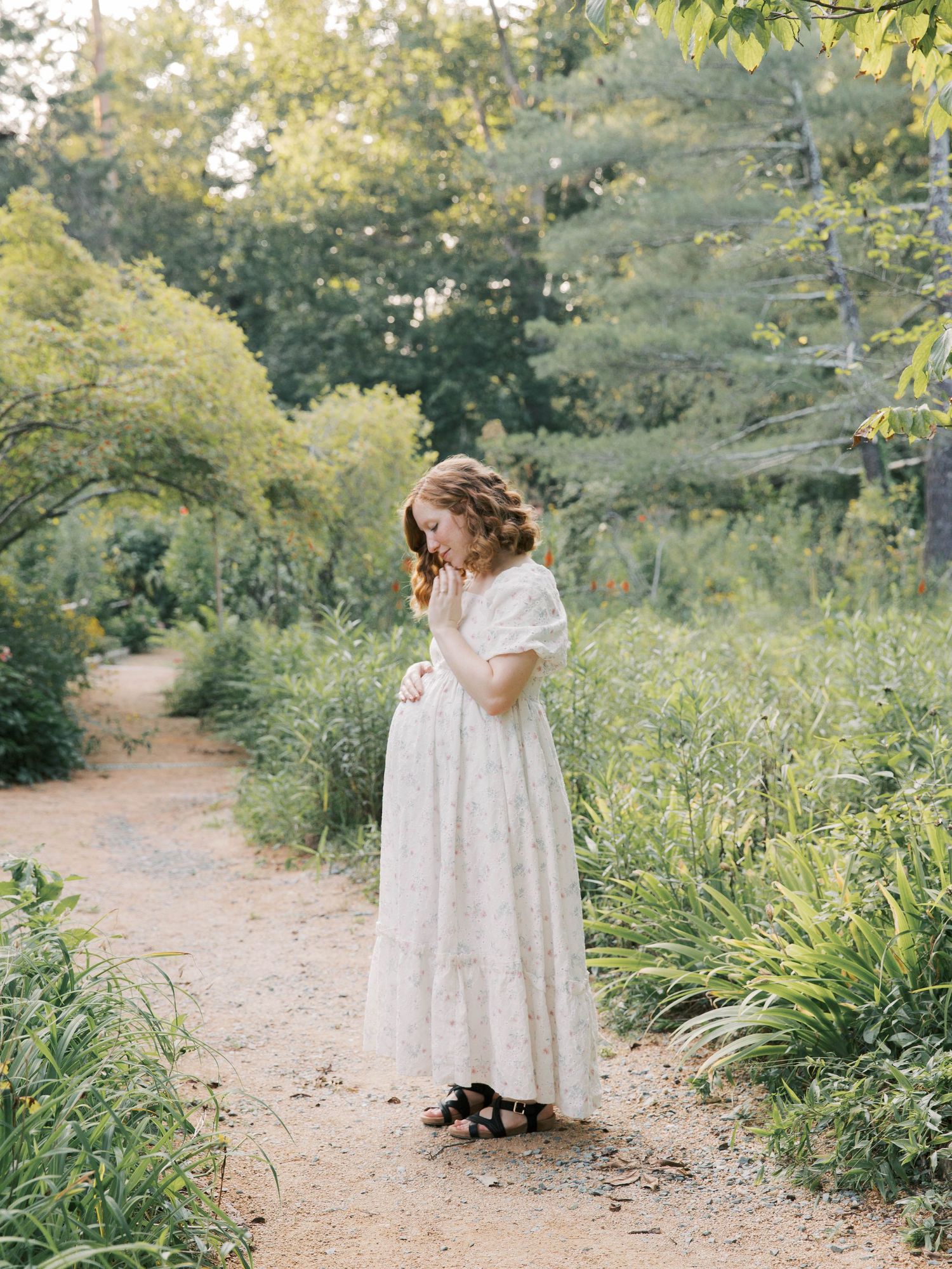 A woman in a white dress stands on a garden path surrounded by lush greenery.