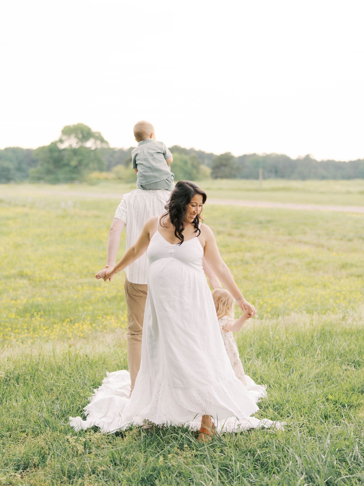 Playful family moment in sunlit field wearing white and beige.