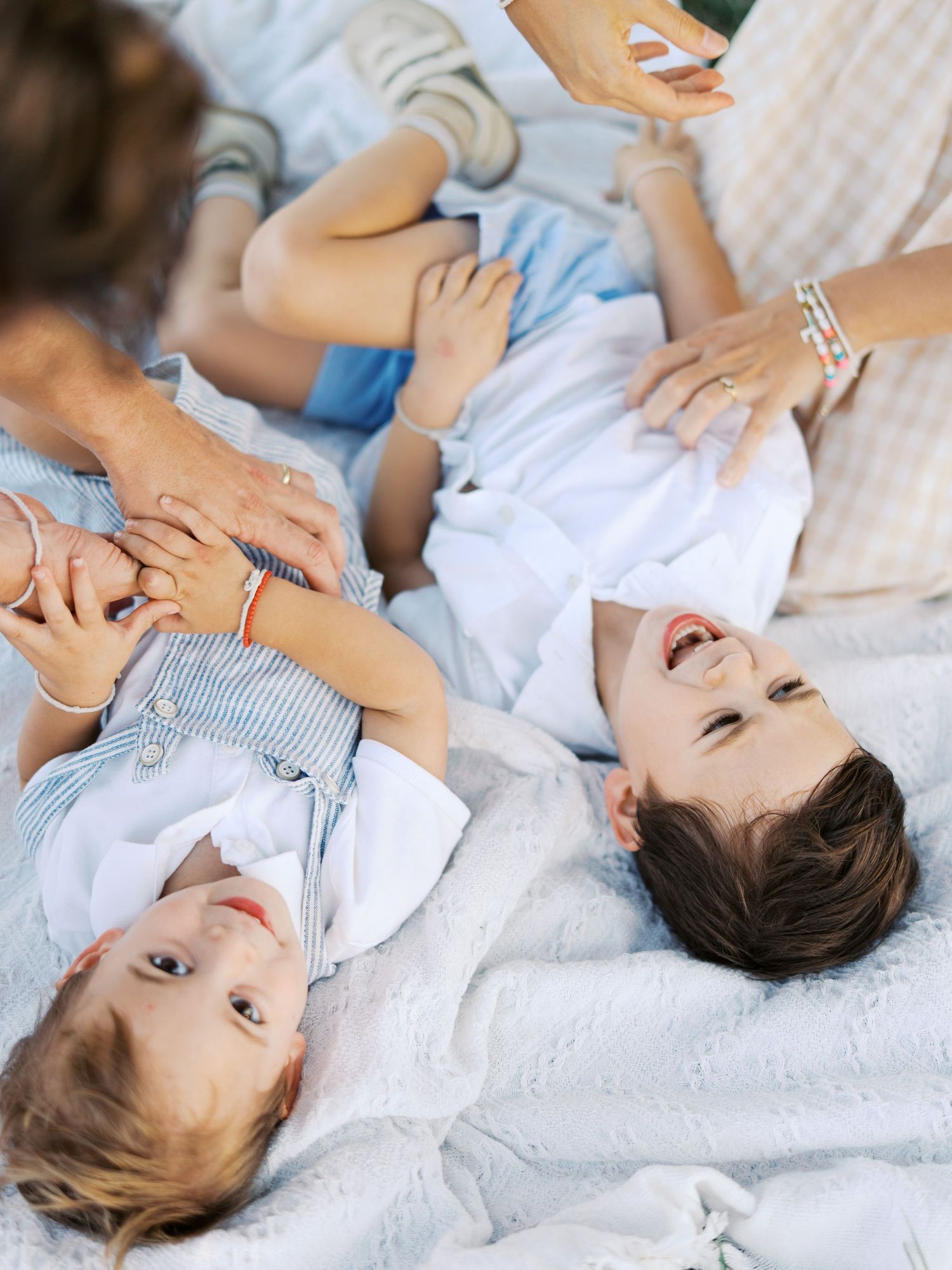 Family members lying together on white bedding while sharing joyful moments during a lifestyle photoshoot.
