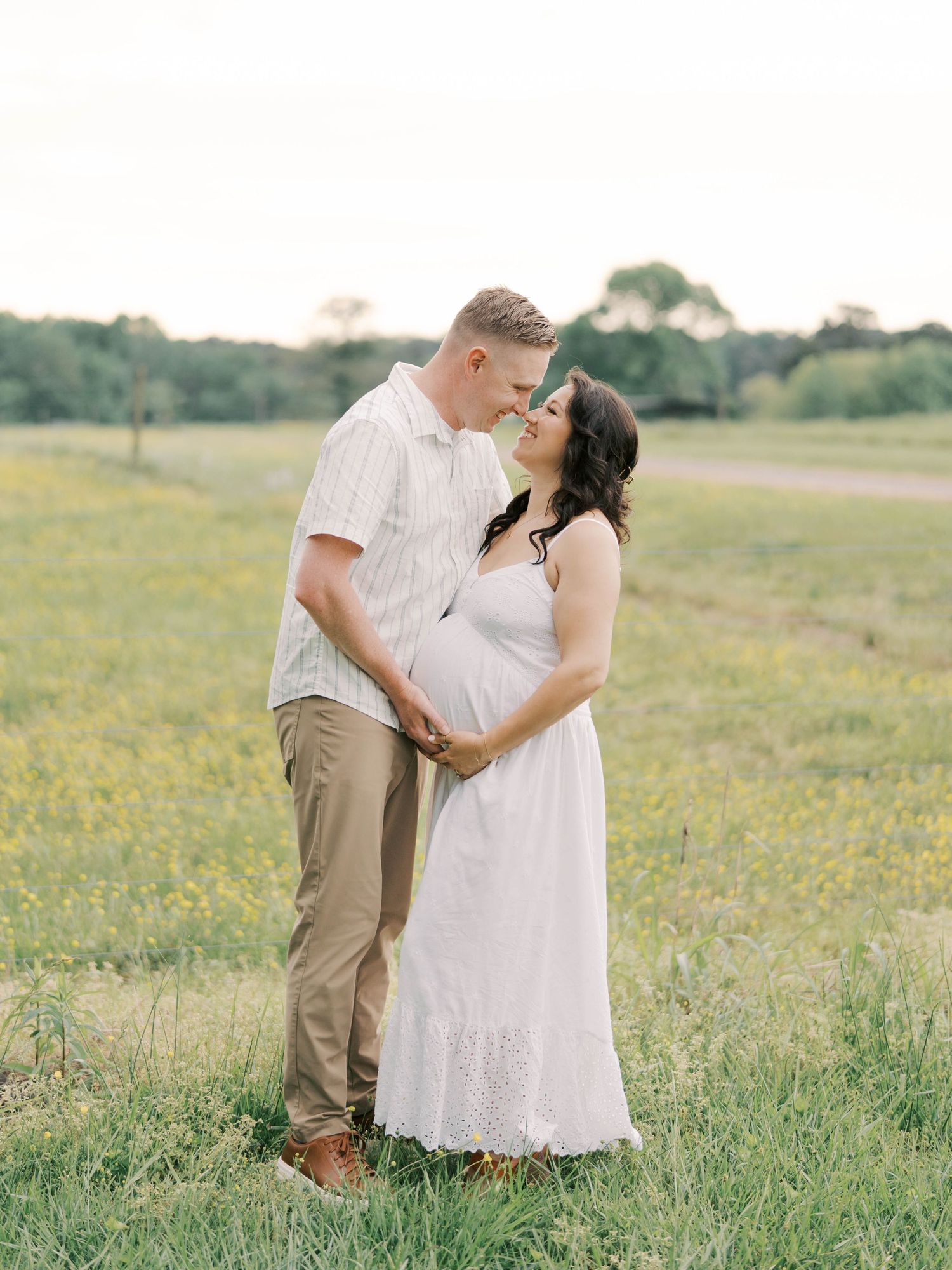 Expecting couple shares an intimate moment in a sunlit meadow during maternity photoshoot.