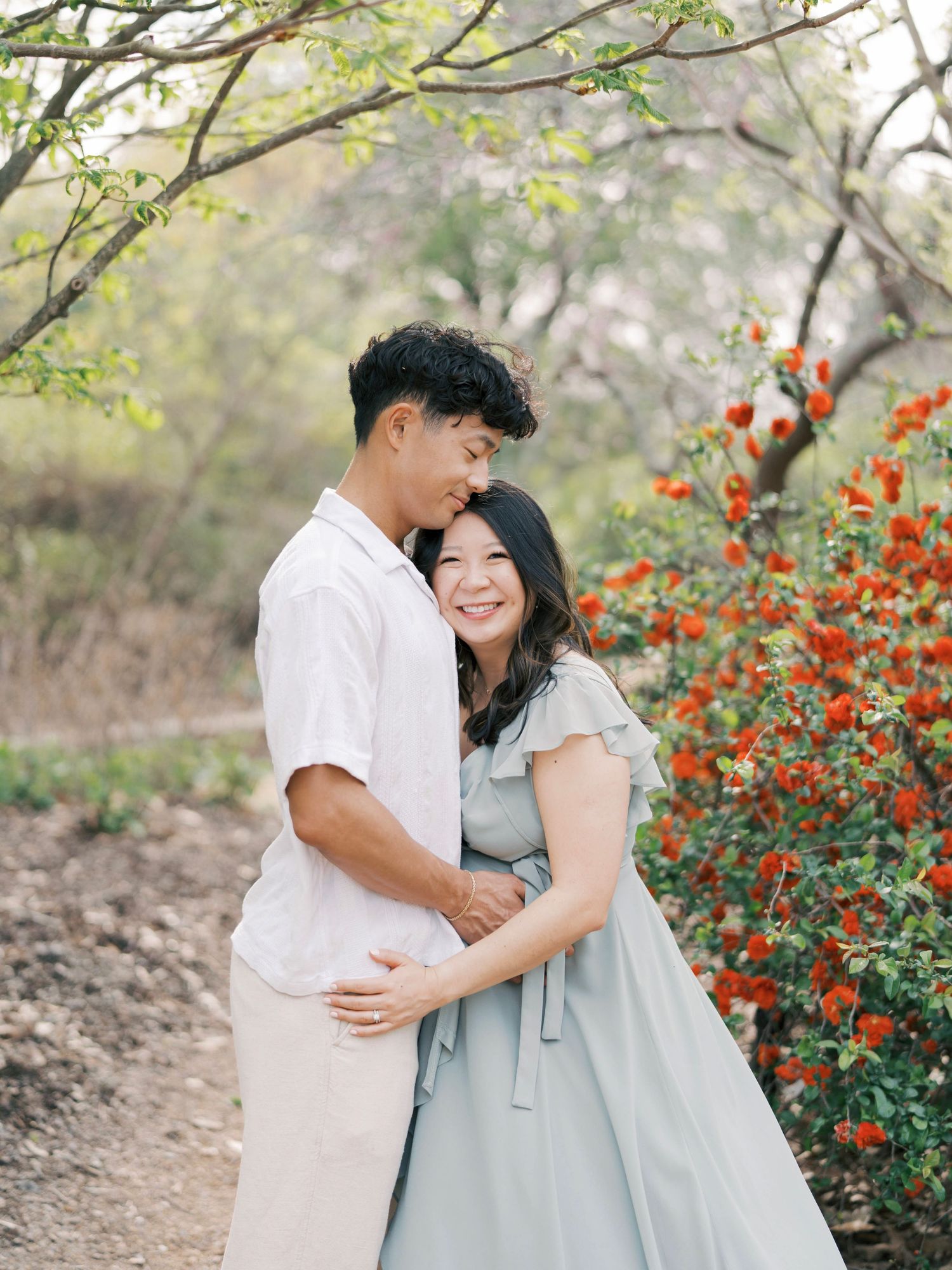 Happy couple embraces near blooming orange flowers during outdoor maternity session.