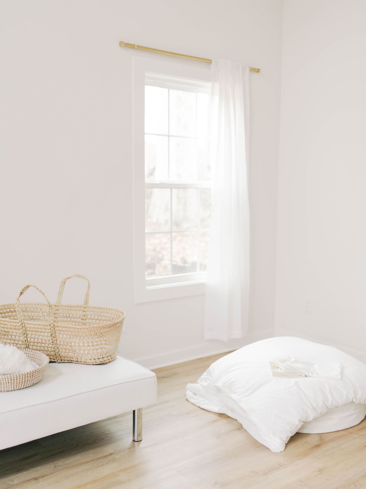 Bright white room with window and baskets on a simple bed frame.