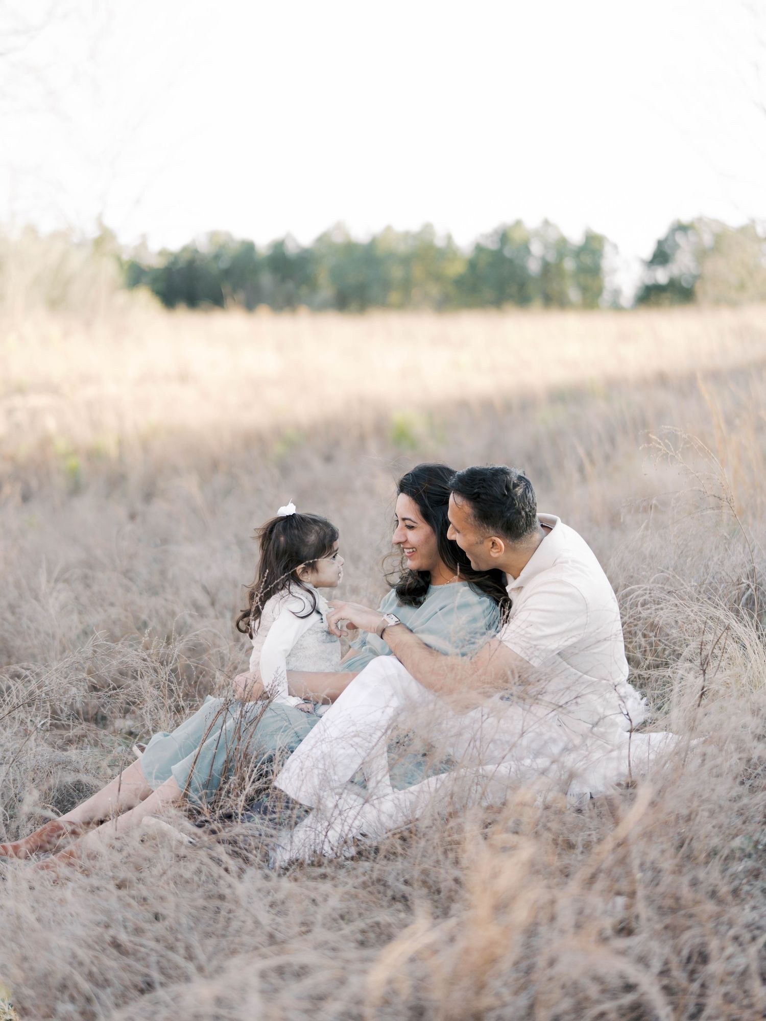 Family of three sitting together in rustic field during golden hour.
