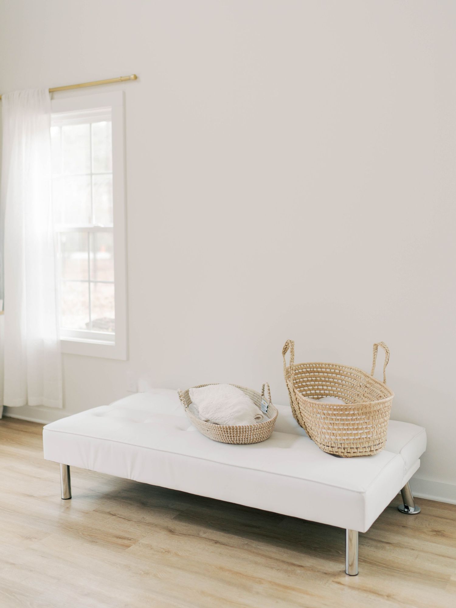 White daybed with woven baskets in a bright minimalist room with hardwood floors.
