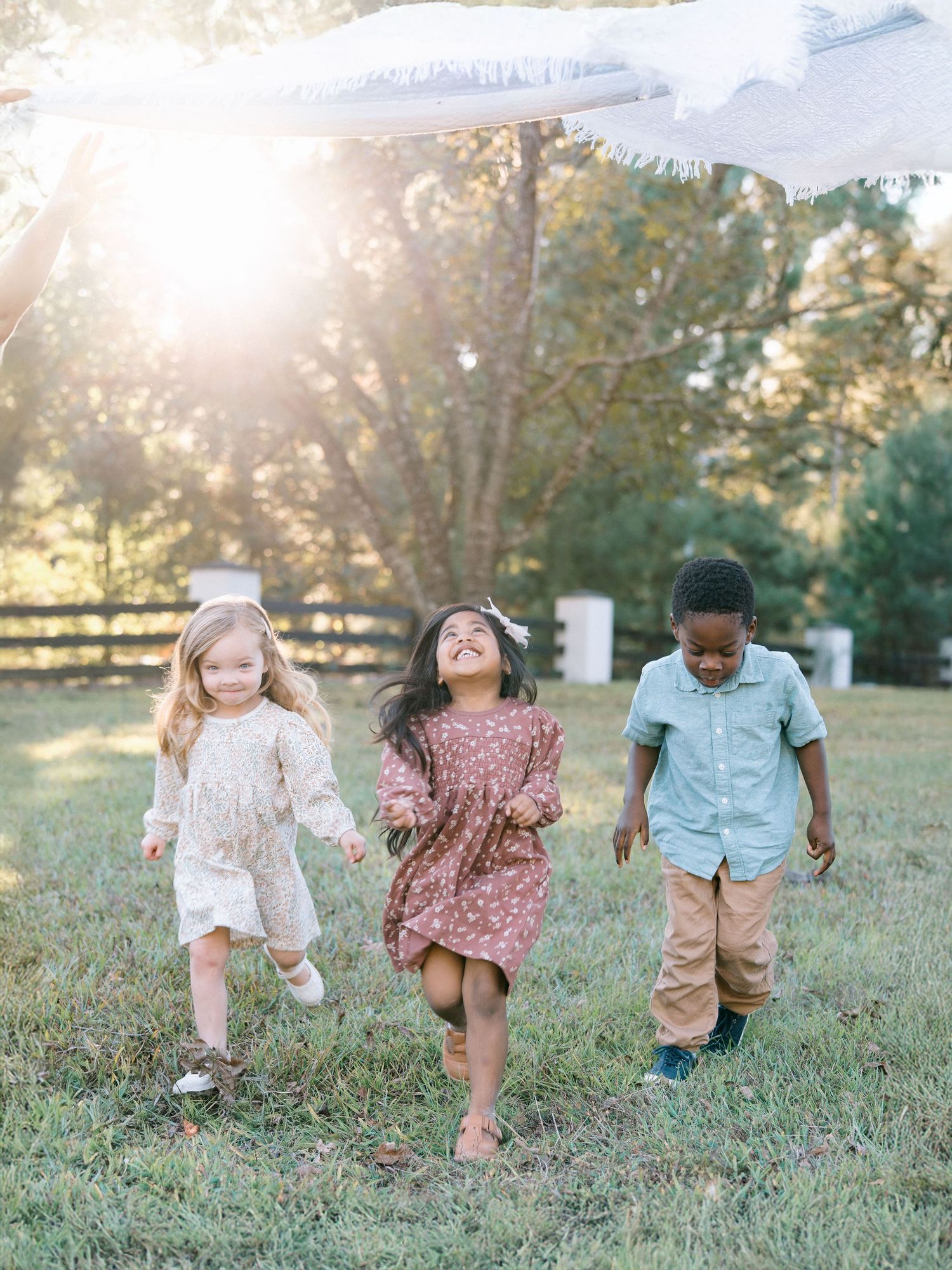 Three happy children running and holding hands in a sunny green field during golden hour.
