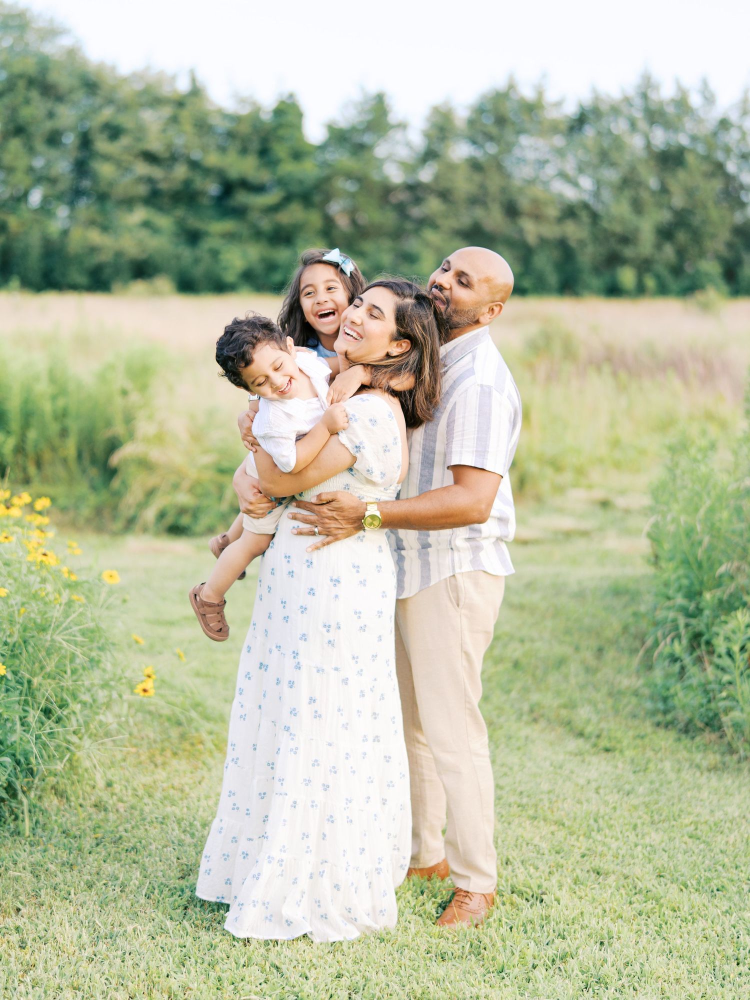 A family shares joyful moments together in a sunny meadow with wildflowers and tall grass.