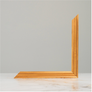 Gold ornate picture frame corner piece displayed on a marble surface against a neutral gray background.