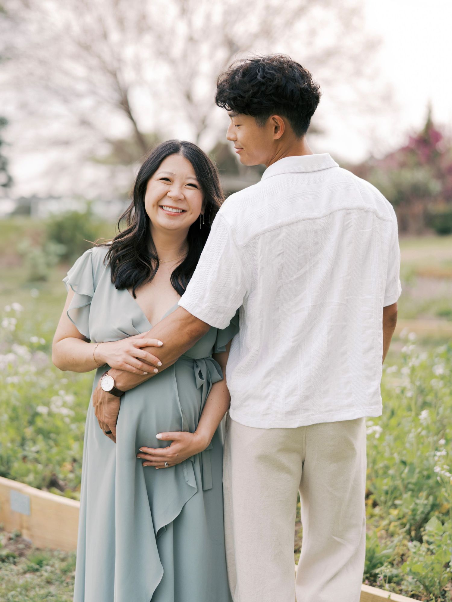 A couple shares an intimate moment in a spring garden with blooming flowers during their maternity session.