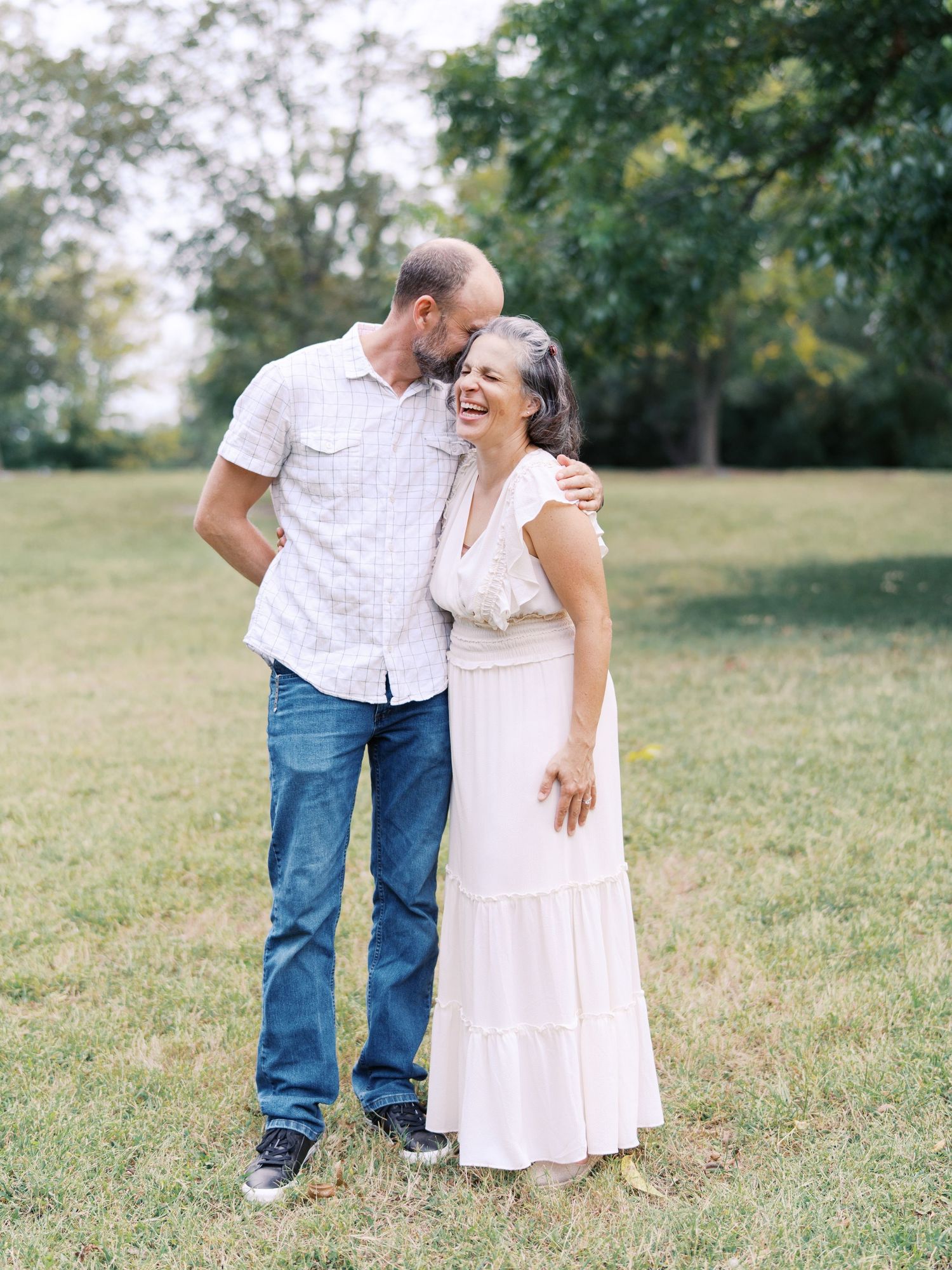 A family embraces and laughs together while standing in a grassy field on a summer afternoon.