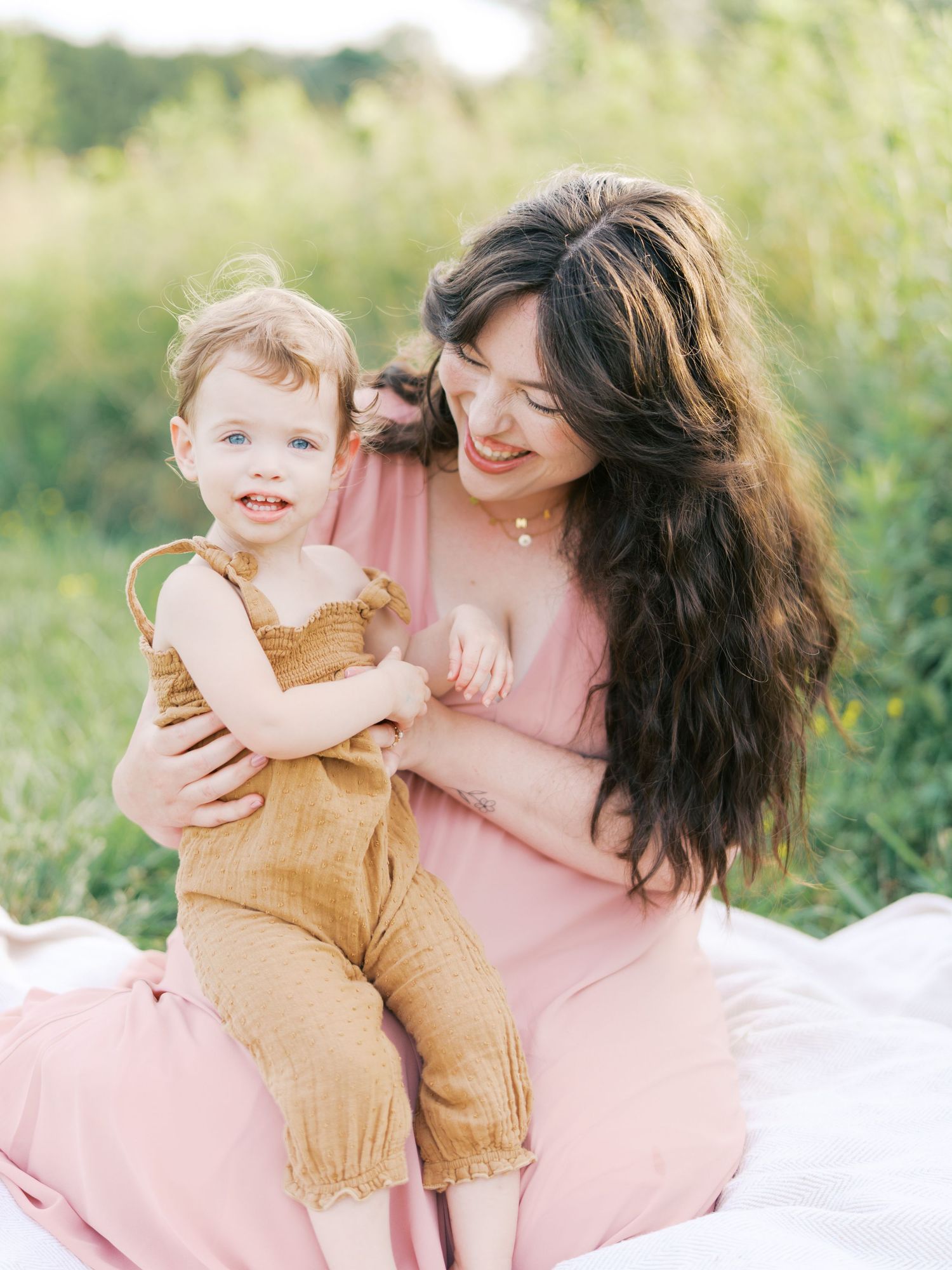Mother and young child in matching pink and yellow outfits play together outdoors in a sunlit meadow.