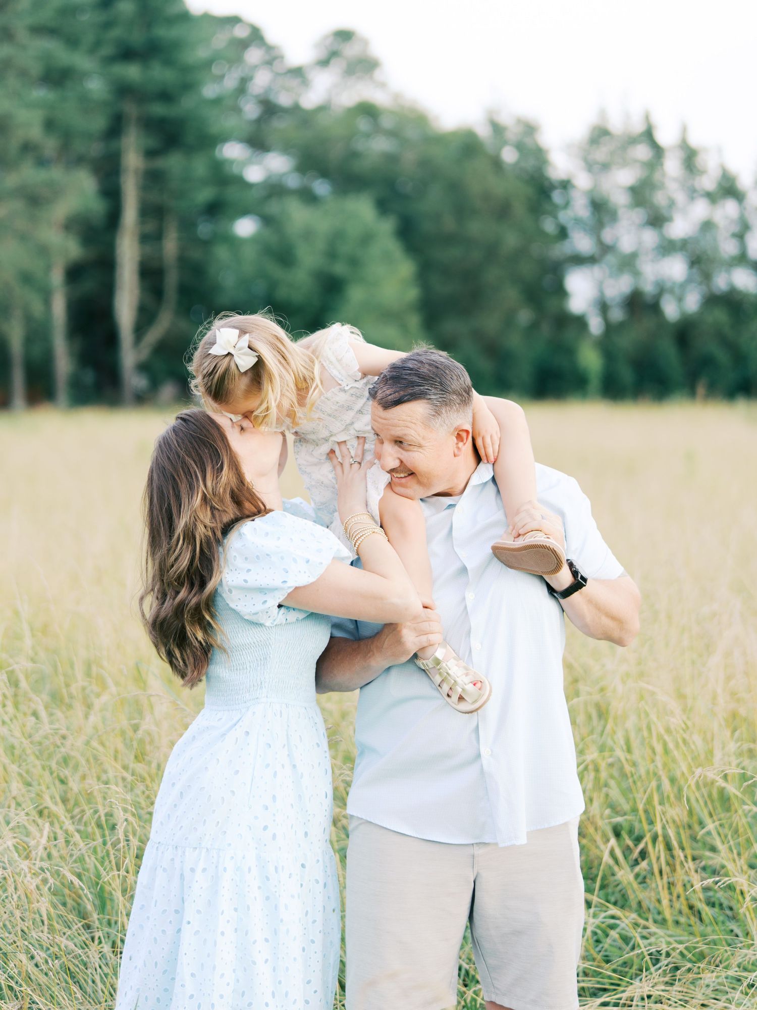 A couple shares romantic moments in a sunlit meadow wearing coordinating white outfits during a summer photoshoot.