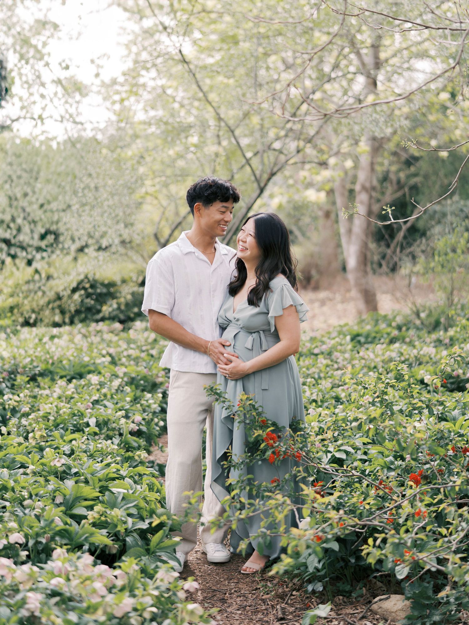 A couple poses along a garden path surrounded by lush greenery and flowering plants.