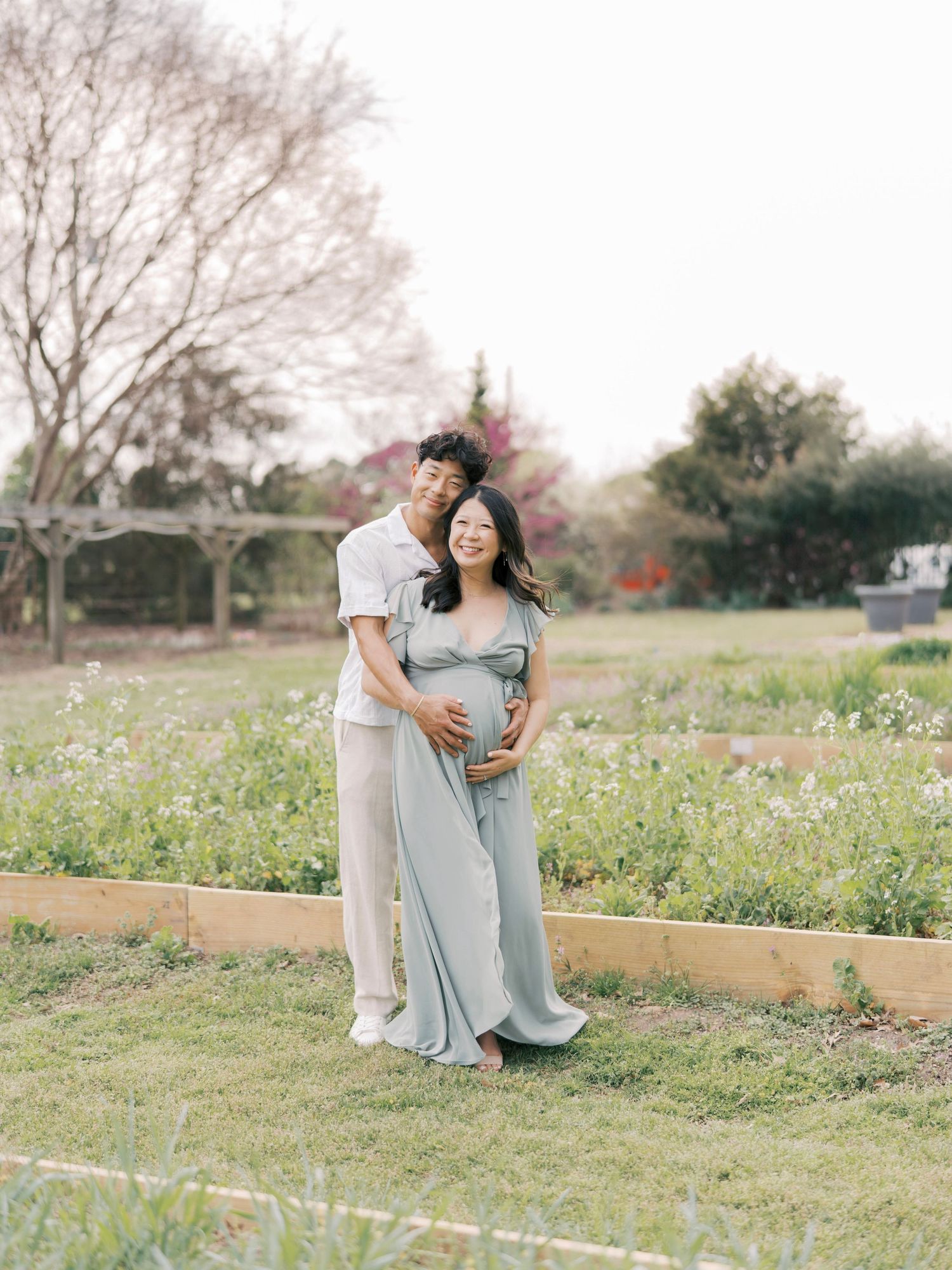 Expecting couple shares intimate moment in garden setting during spring photoshoot.