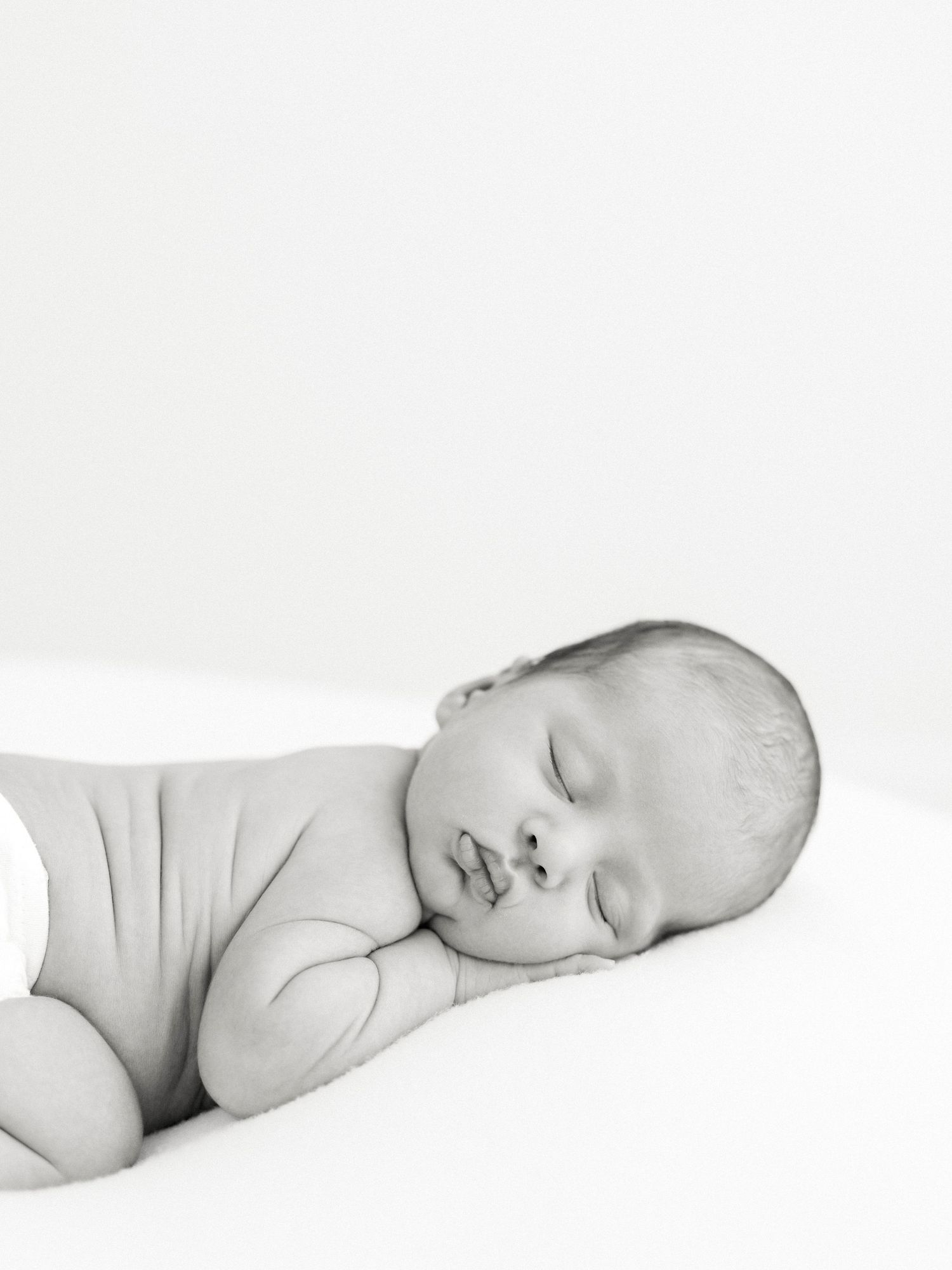 Peaceful newborn baby sleeping soundly, wrapped in soft gray, captured in elegant black and white photography.