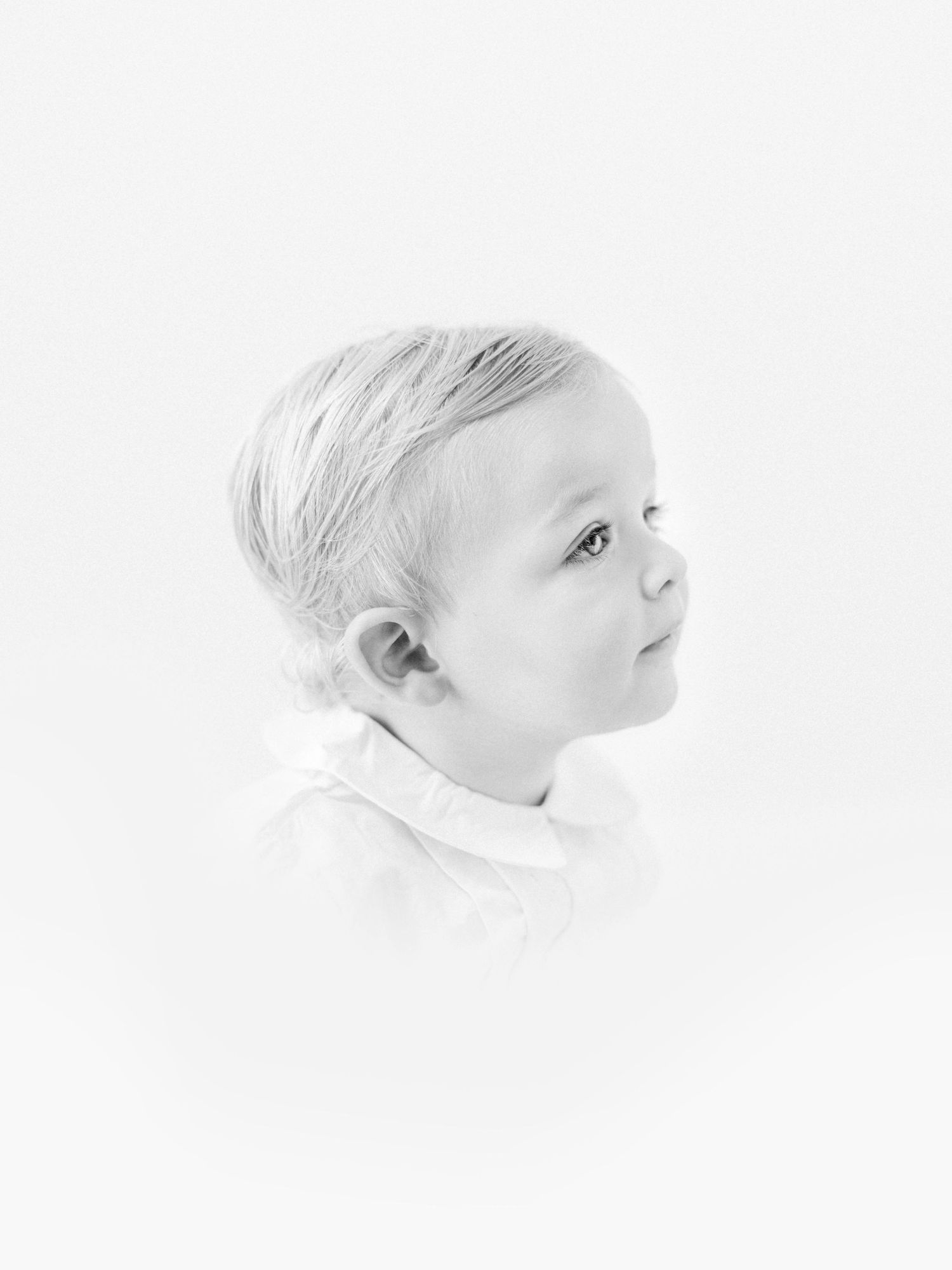 Black and white portrait of a young toddler with light hair gazing upward against a white background.