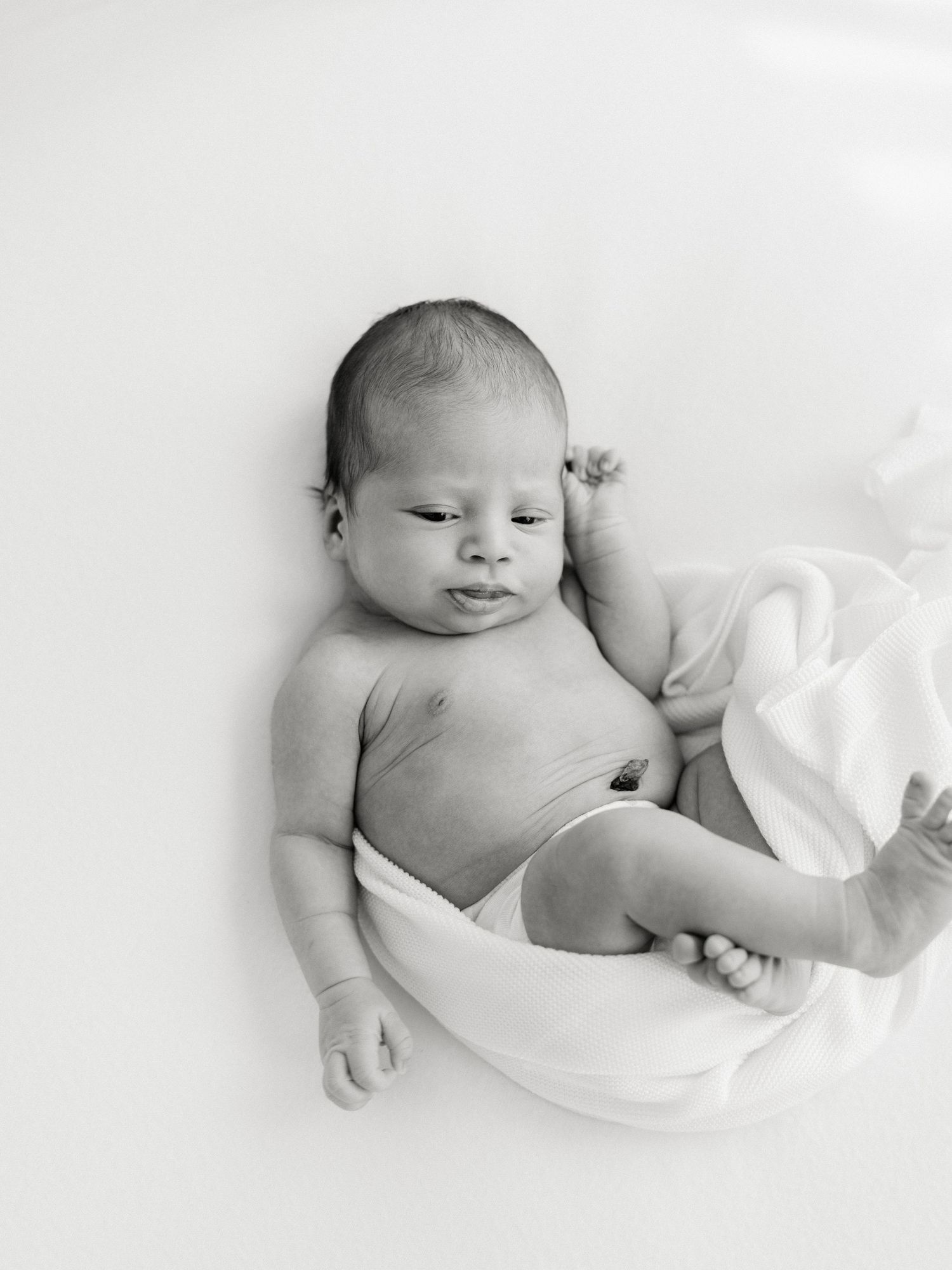 Black and white newborn baby photo of an infant lying on a white blanket, eyes slightly open after visiting baby boutiques in Raleigh