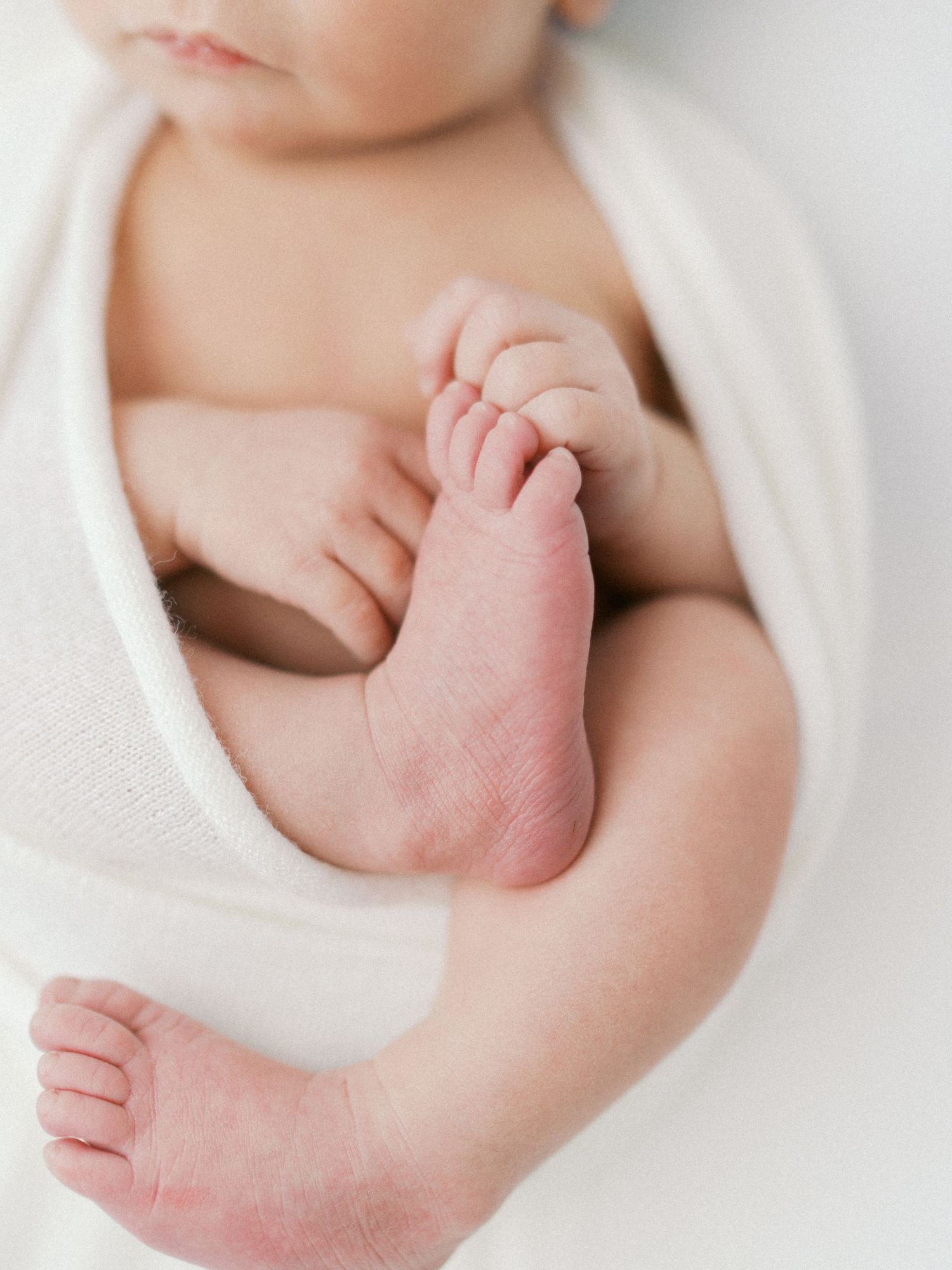 Close-up of a swaddled newborn baby's tiny feet and toes wrapped in a soft white blanket.