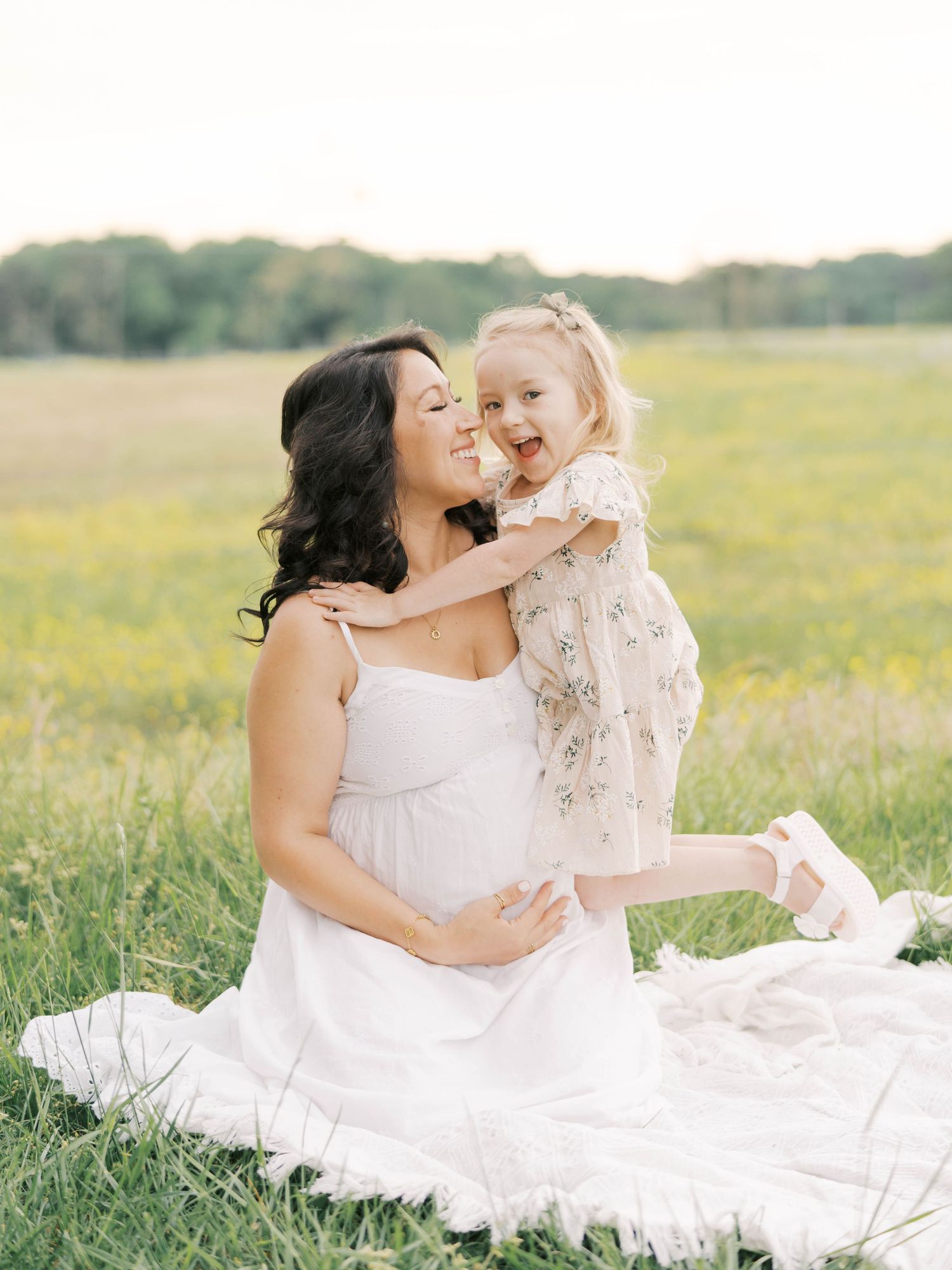 Sweet moment between mother and child sitting on white blanket in meadow.