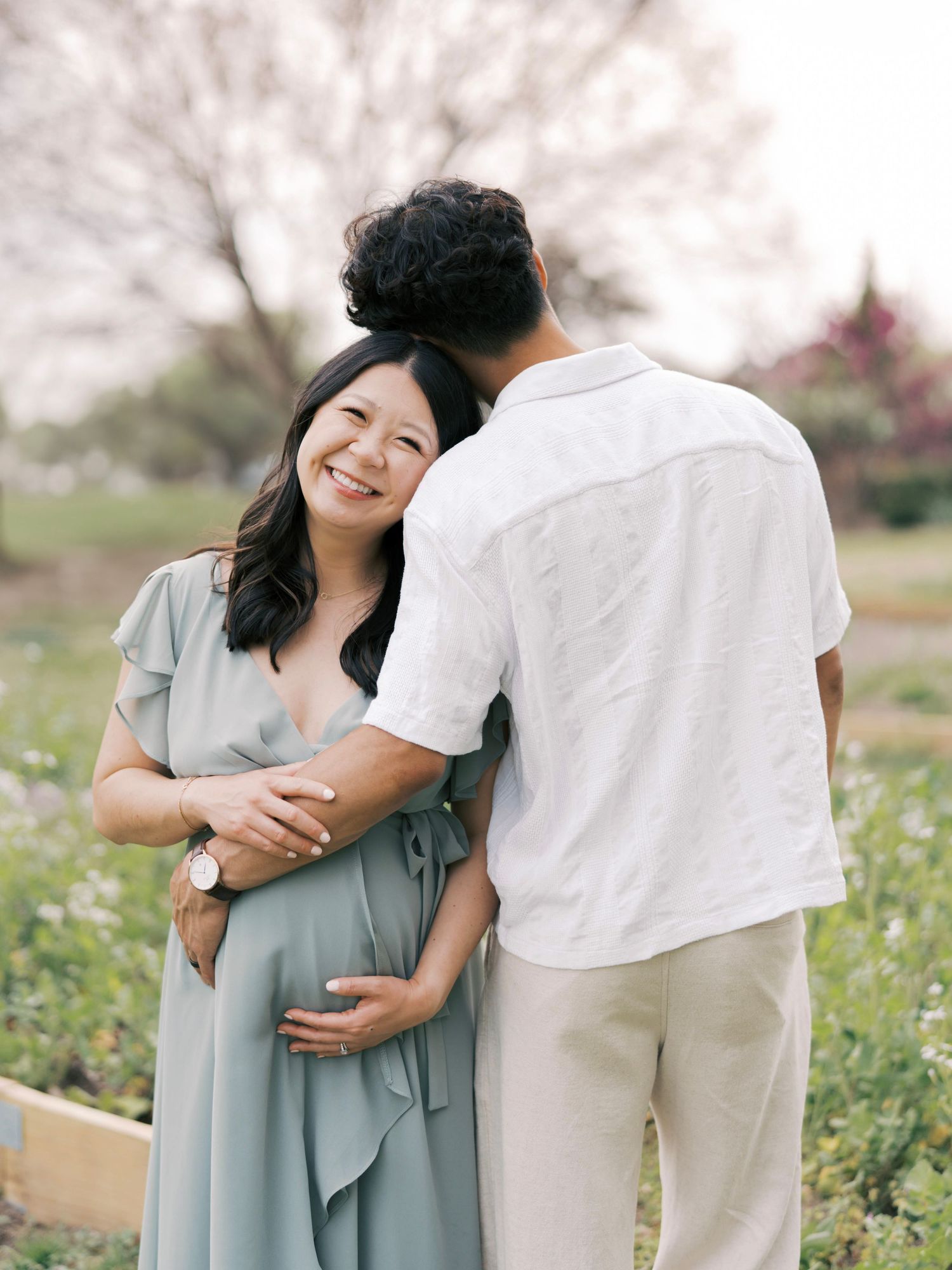 Tender moment between couple in garden setting during maternity photoshoot.