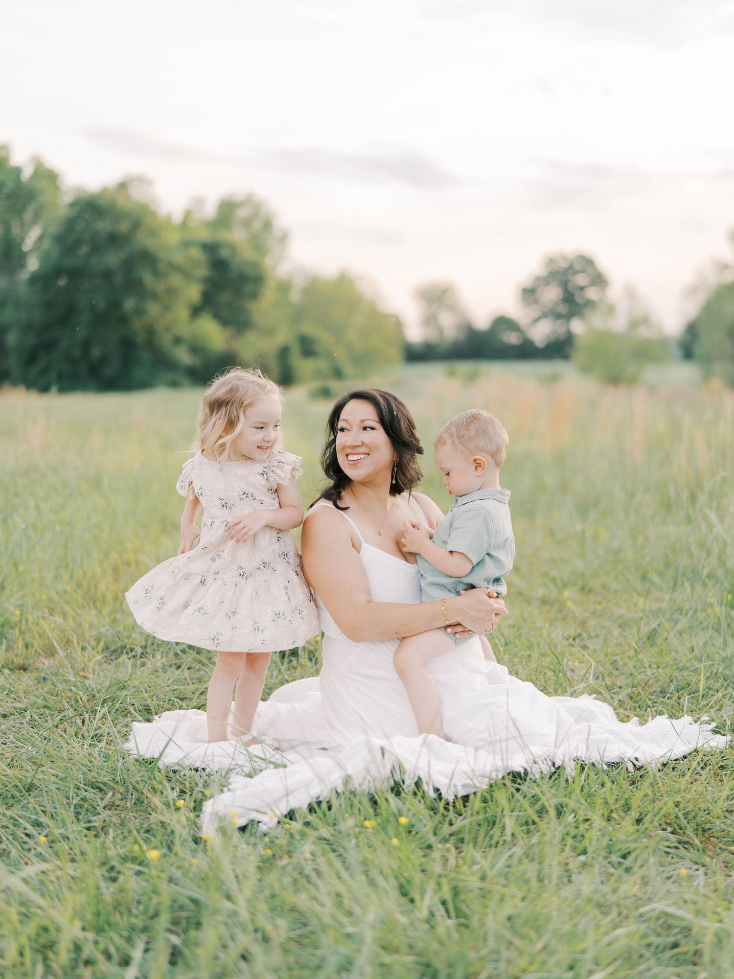 Family sitting together on white blanket in summer meadow.