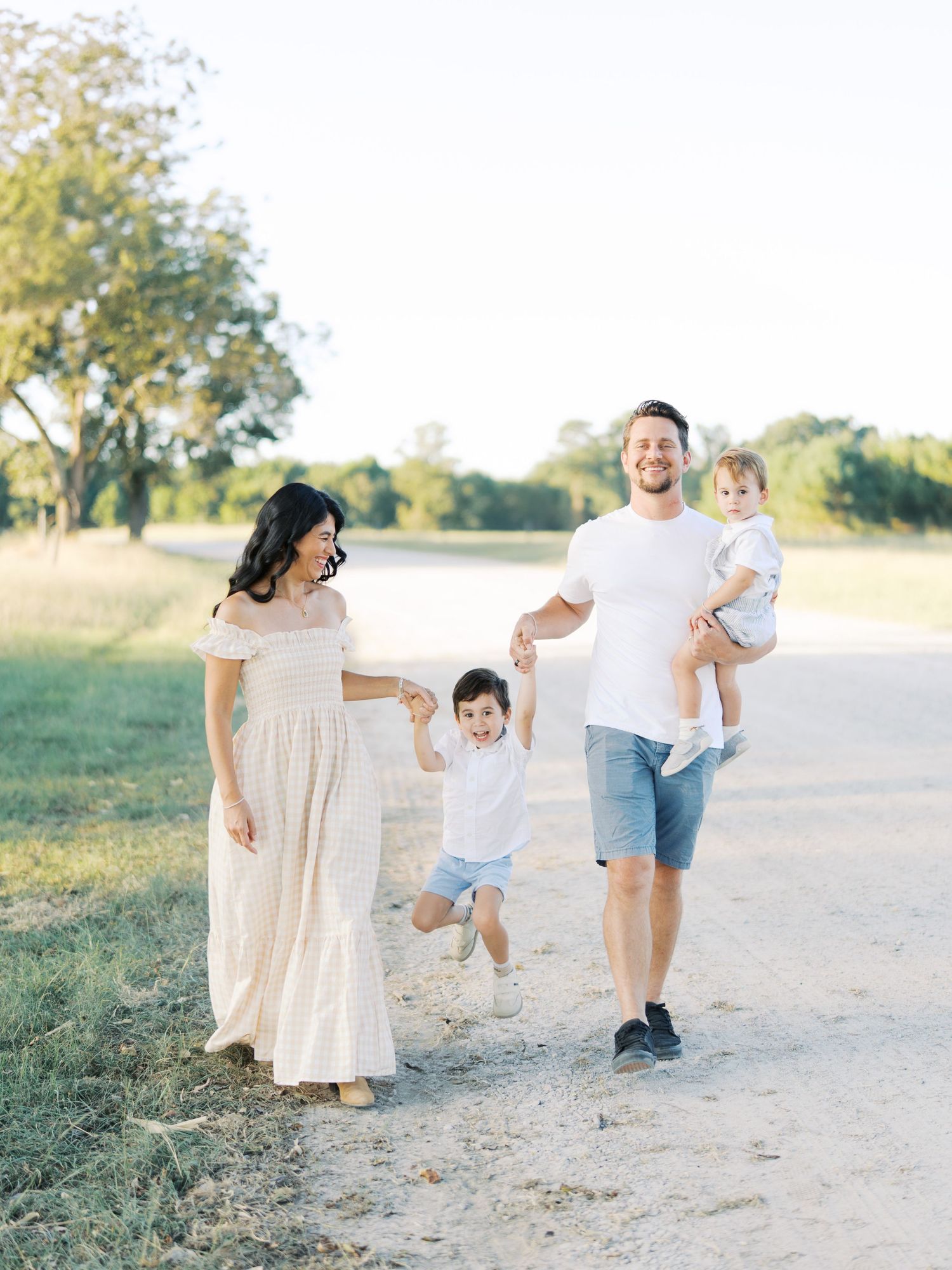A family walks together on a dirt path through a sunny field on a warm summer day.