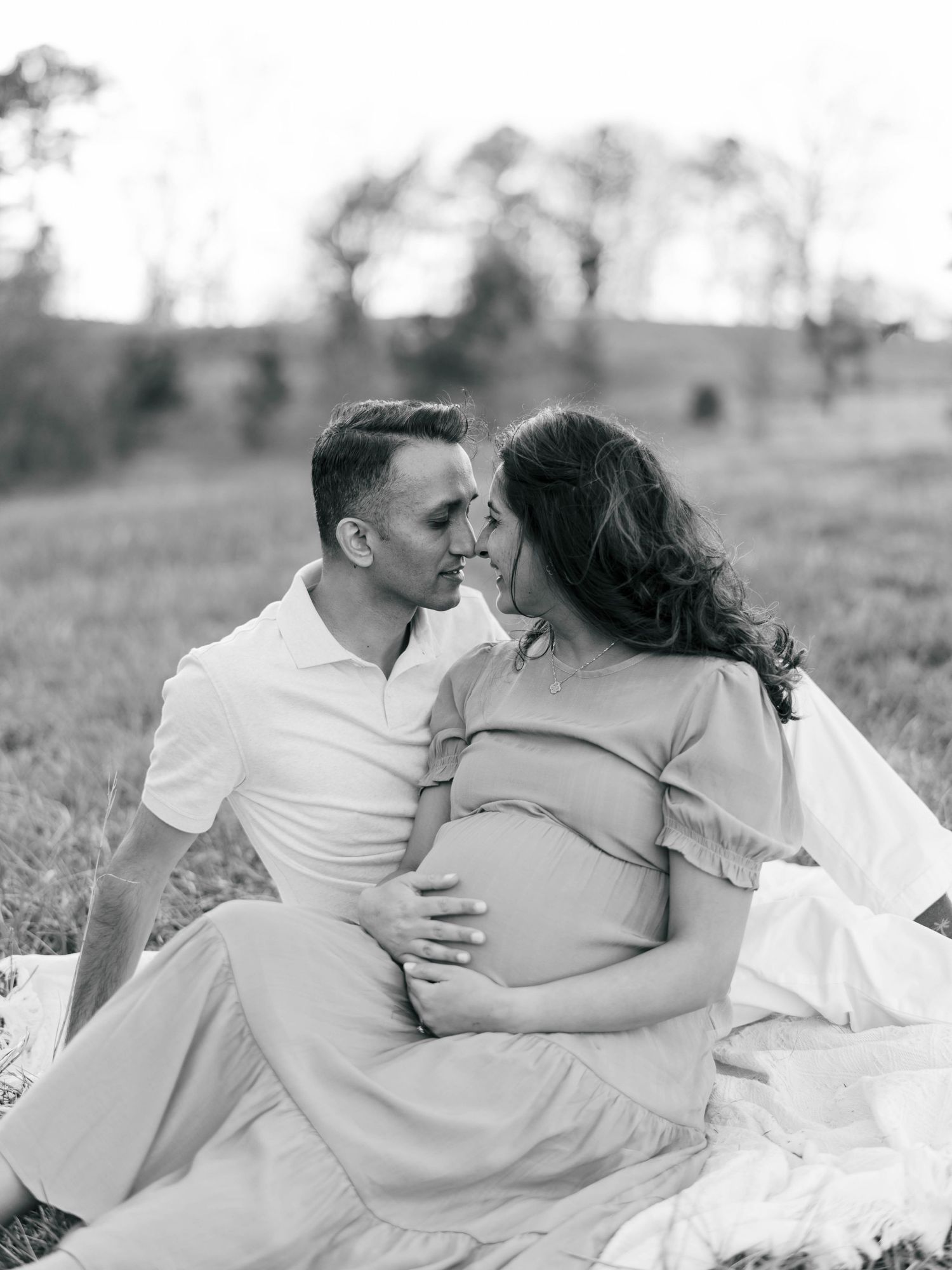 Black and white image of couple sharing intimate moment on blanket in field.
