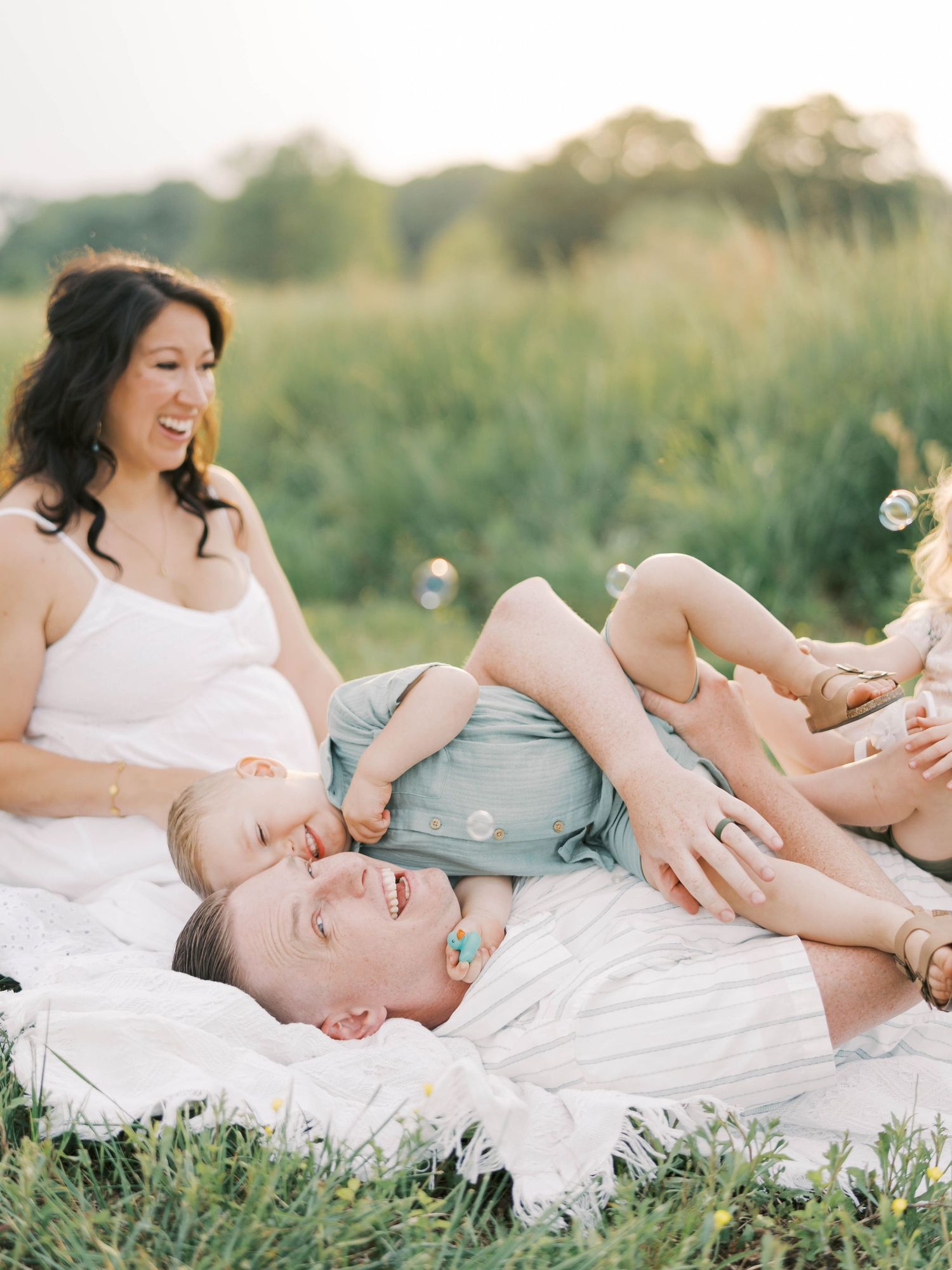 A couple lying in a grassy meadow sharing a playful moment with bubbles on a sunny summer day.