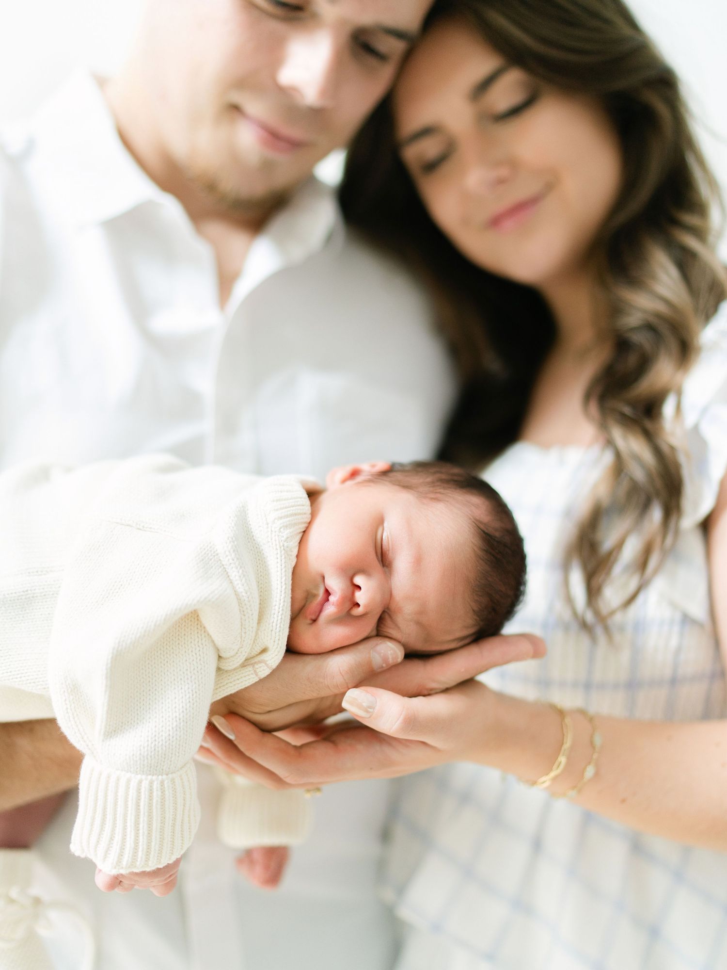 Parents tenderly cradle their sleeping newborn baby together in a bright, intimate family portrait session.