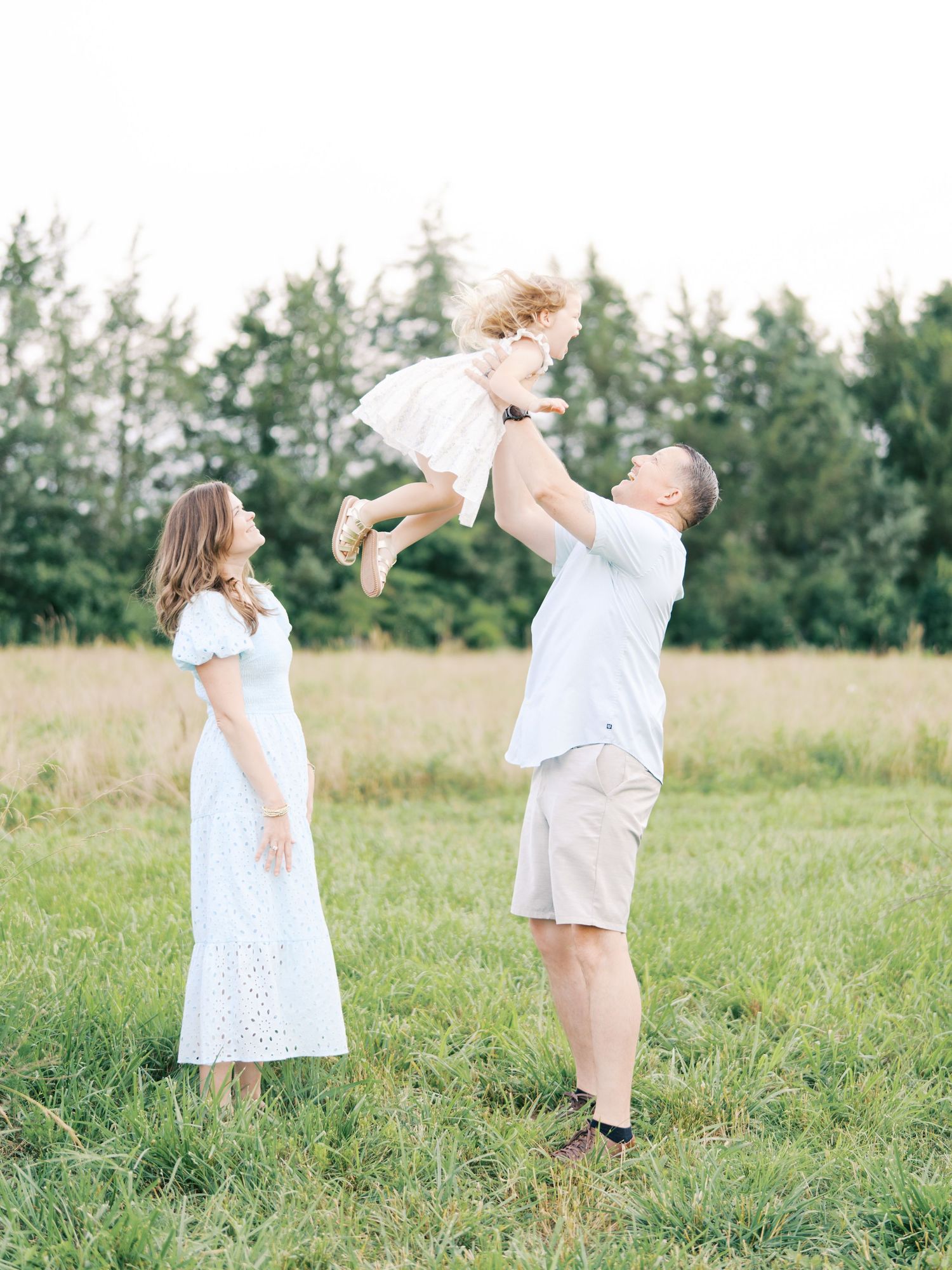 Children in white outfits play together in a sunny grassy field during a summer photoshoot.