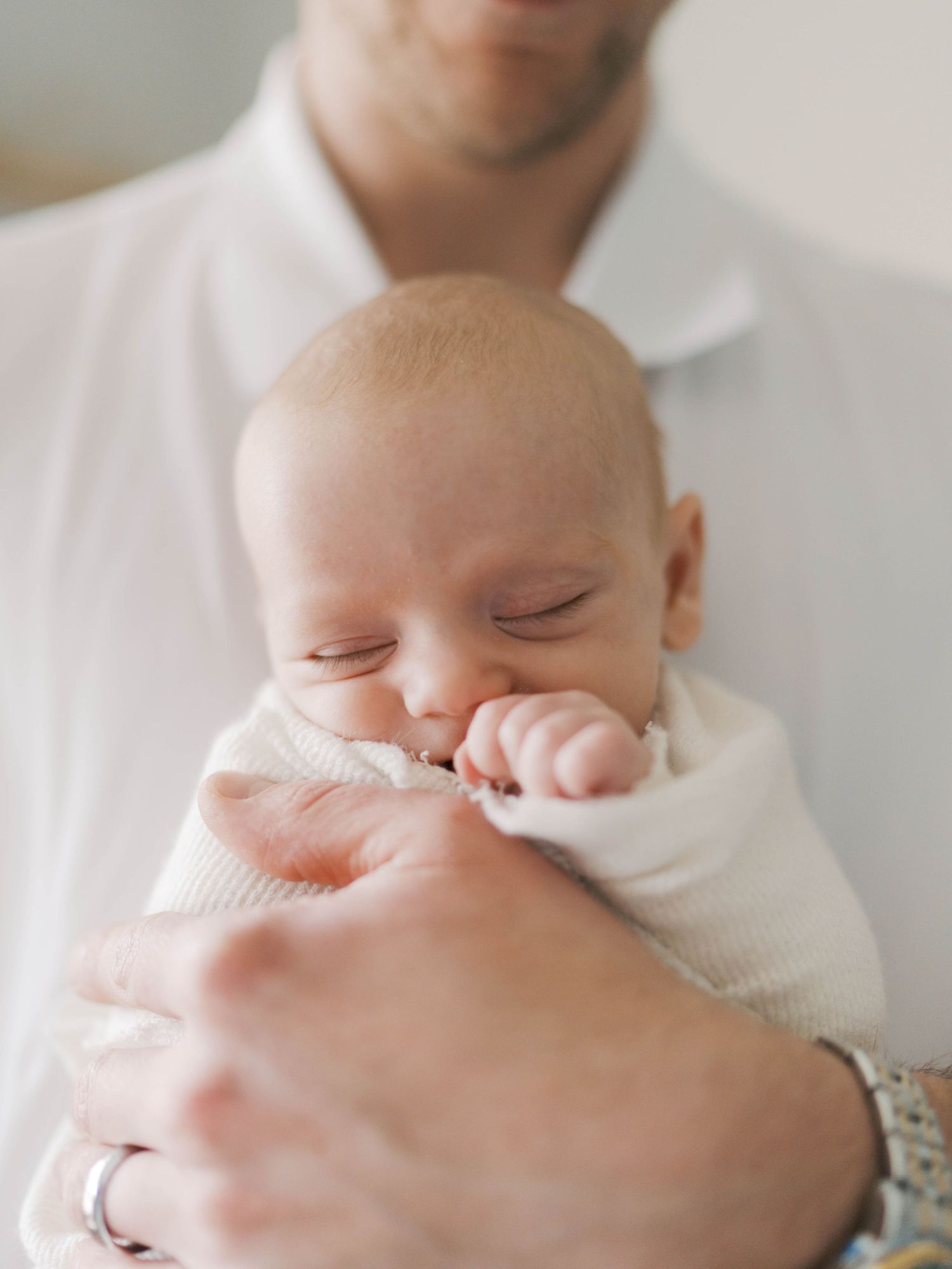 A newborn baby sleeping peacefully while being cradled in an adult's hands, wearing a white outfit.