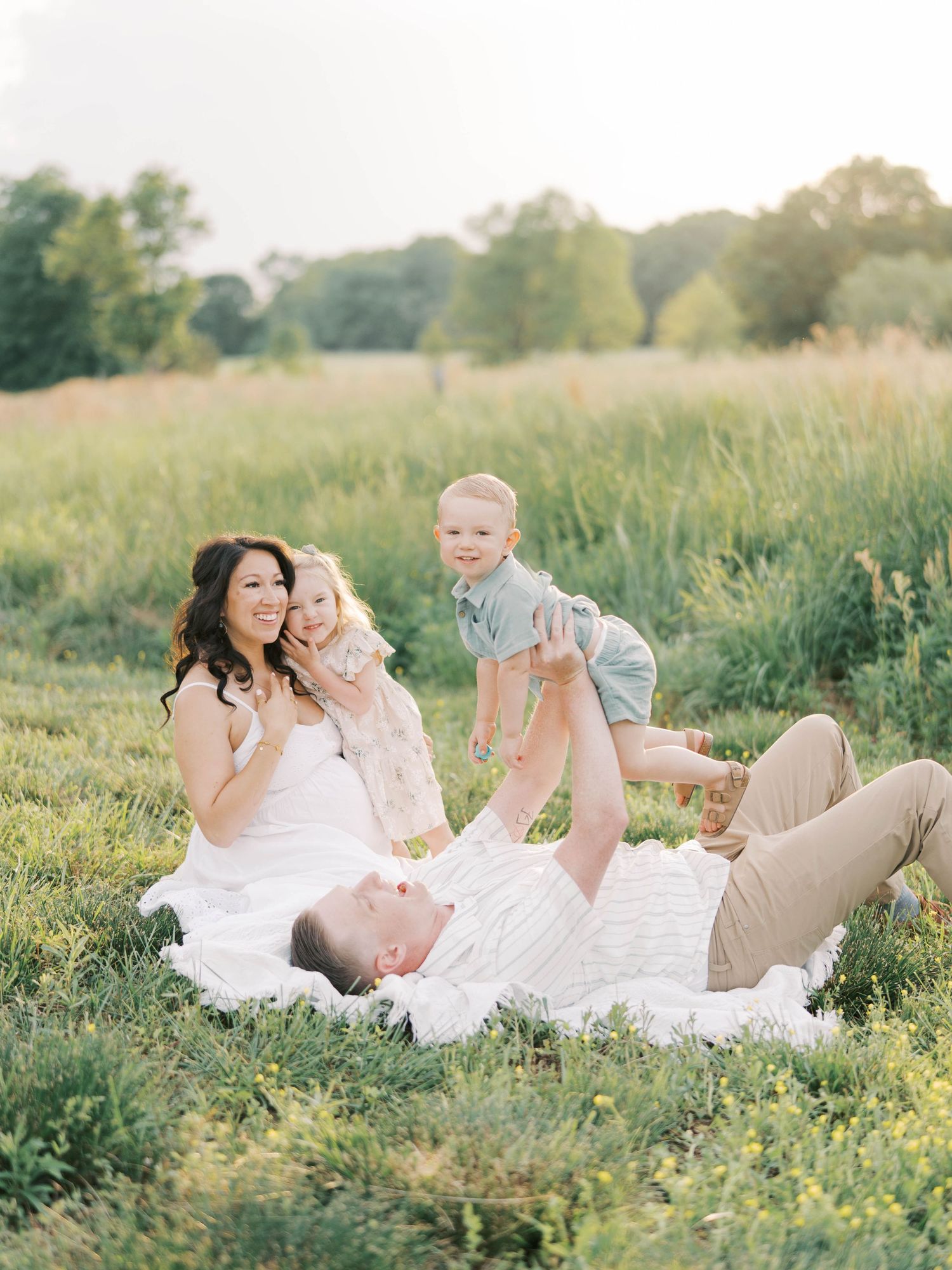 Happy family playing together on blanket in wildflower meadow at sunset.