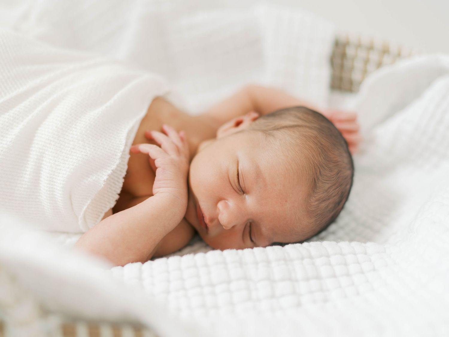 Peaceful newborn baby sleeping wrapped in soft white blanket on textured white surface.