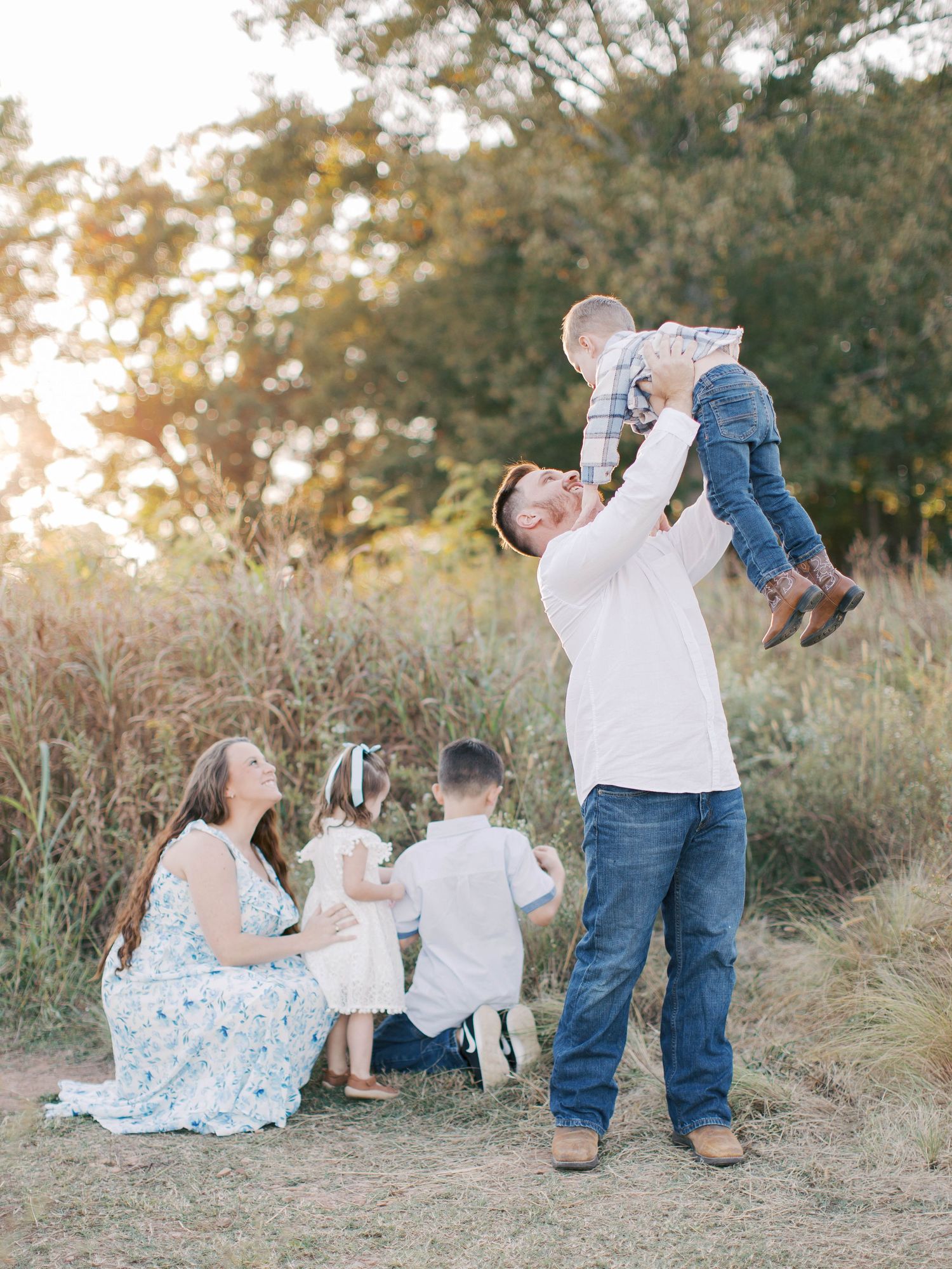 Family enjoying sunset outdoors with children playing and parents sitting on grass.