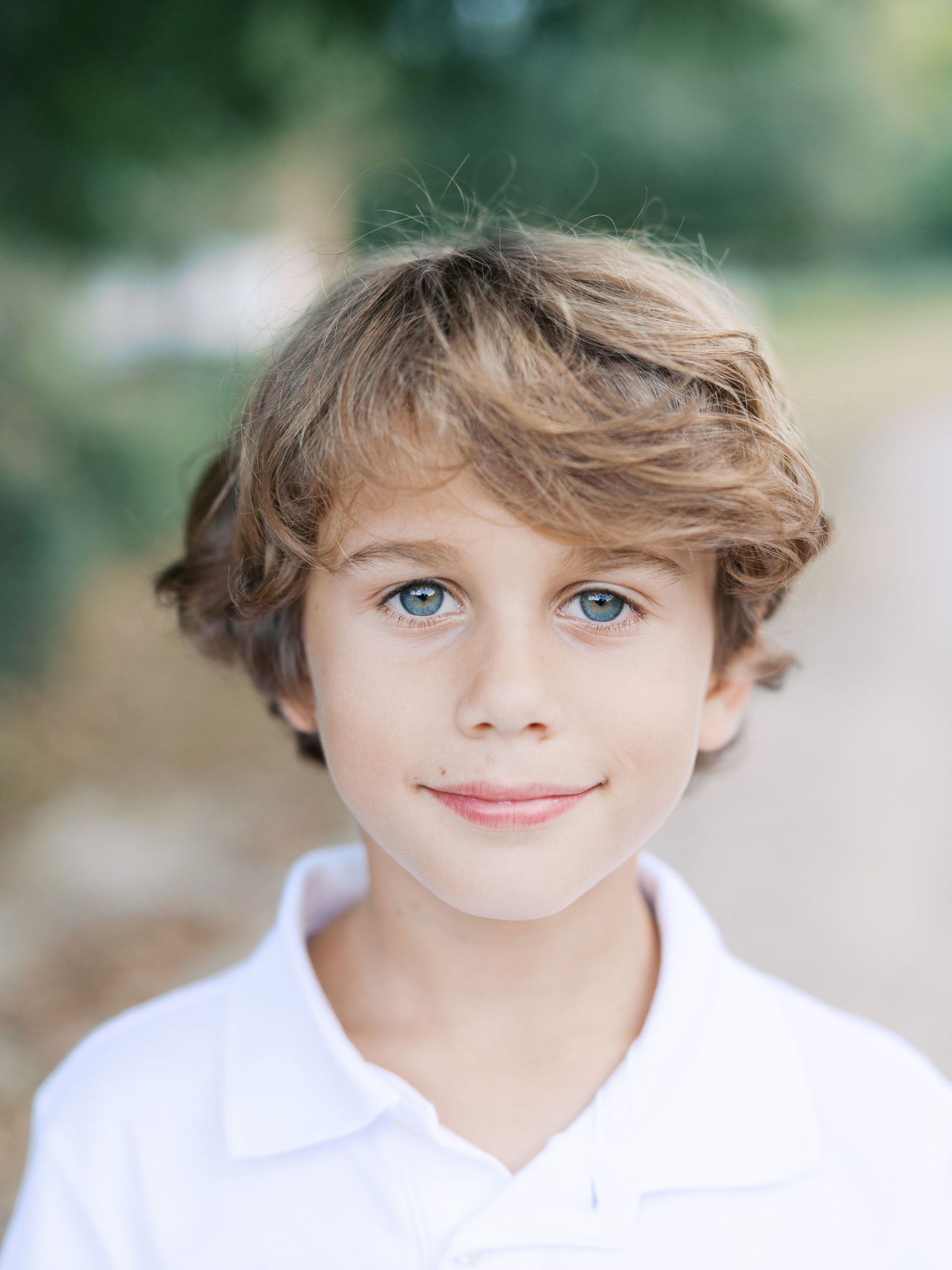 A young child in a white polo shirt smiles at the camera with tousled brown hair and bright eyes.
