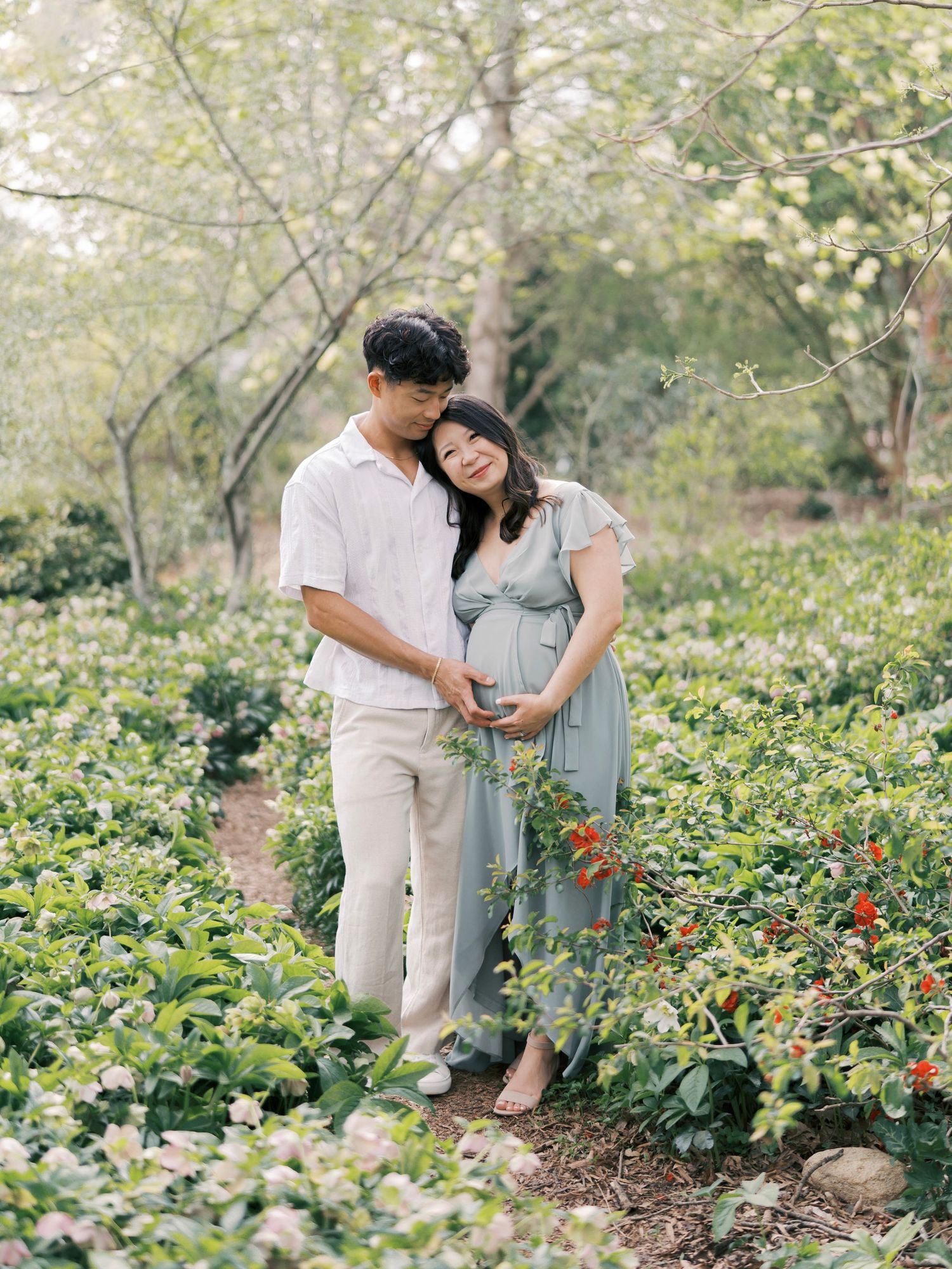 A couple embraces among blooming garden flowers during their outdoor maternity photoshoot.