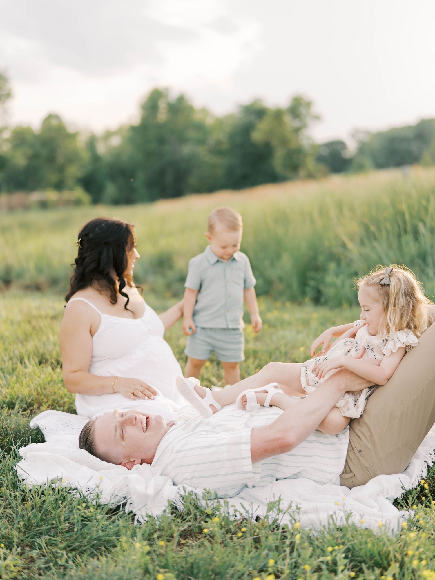 Family enjoying a picnic together on a white blanket in a grassy field.