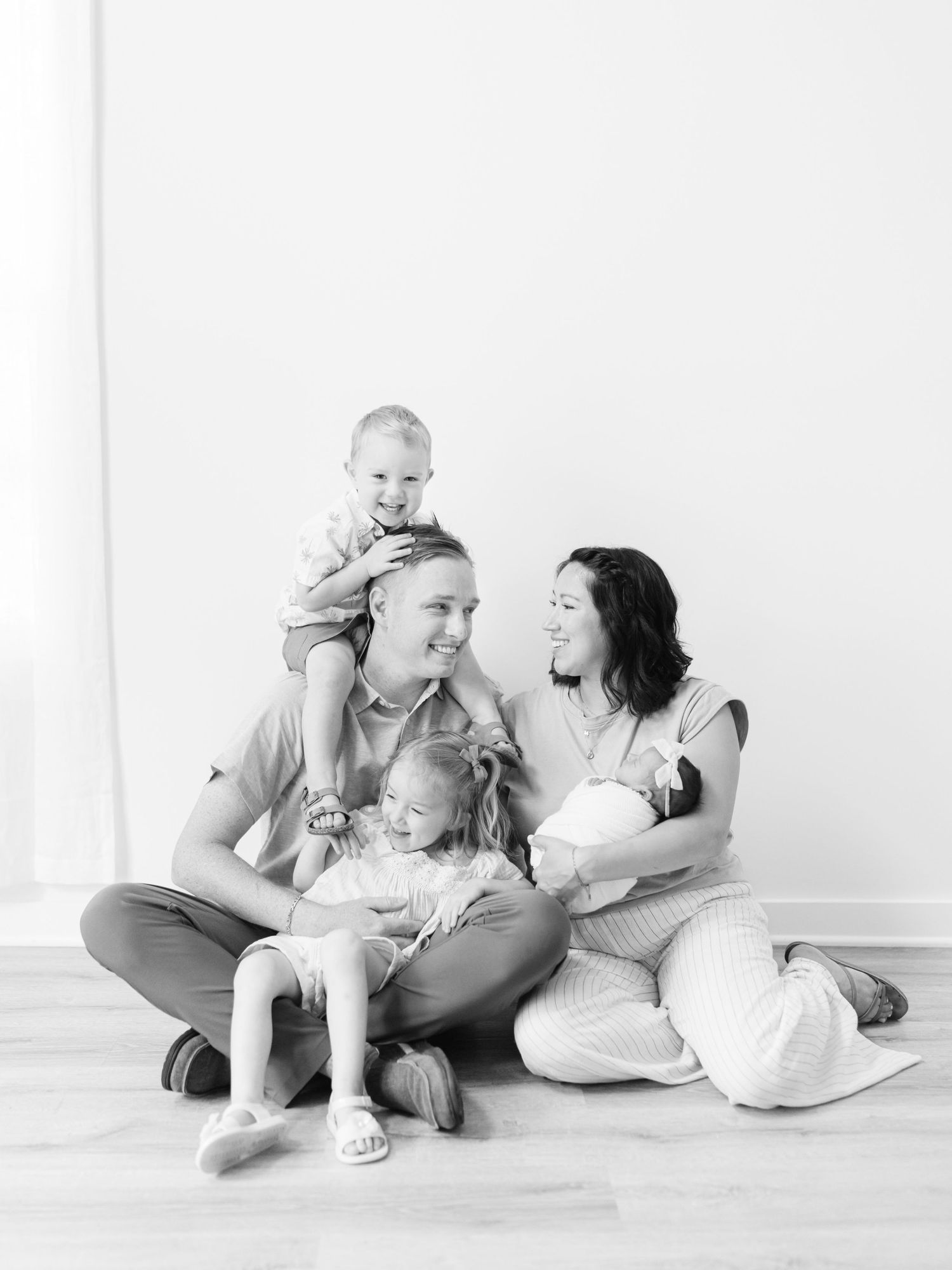 Black and white family photo of two mothers sitting on floor with three young children, including a newborn baby.